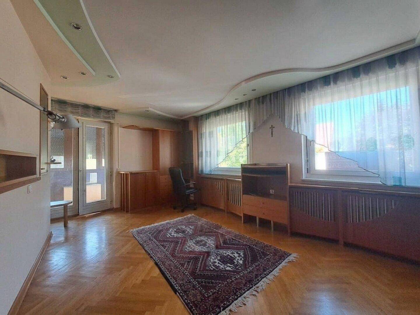 Geräumiges Wohnzimmer mit Parkettboden, großen Fenstern und Zugang zu einem Balkon.