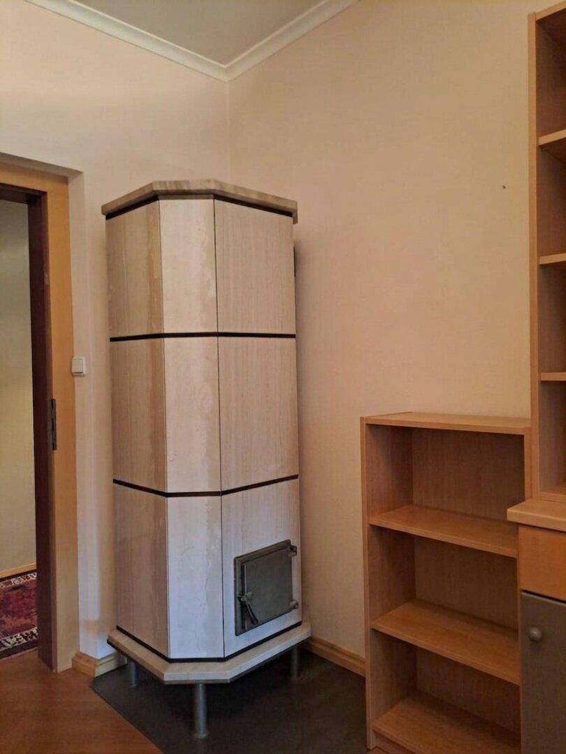 Gemütlicher Raum mit einem traditionellen Kachelofen und Holzregalen, strahlt Wärme aus.
