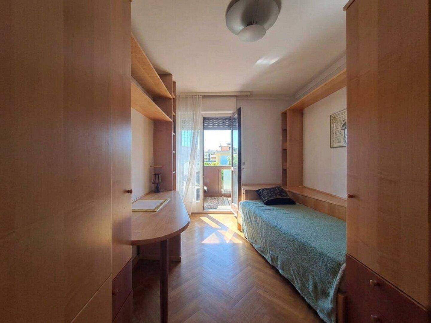Helles Schlafzimmer mit Parkettboden, Einbauschränken und Zugang zu einem kleinen Balkon.
