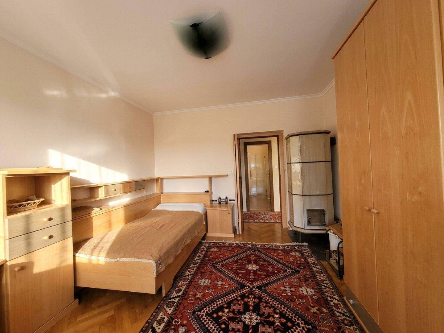 Schlafzimmer mit Parkettboden, Kachelofen und Holzmöbeln, bietet eine warme Atmosphäre.
