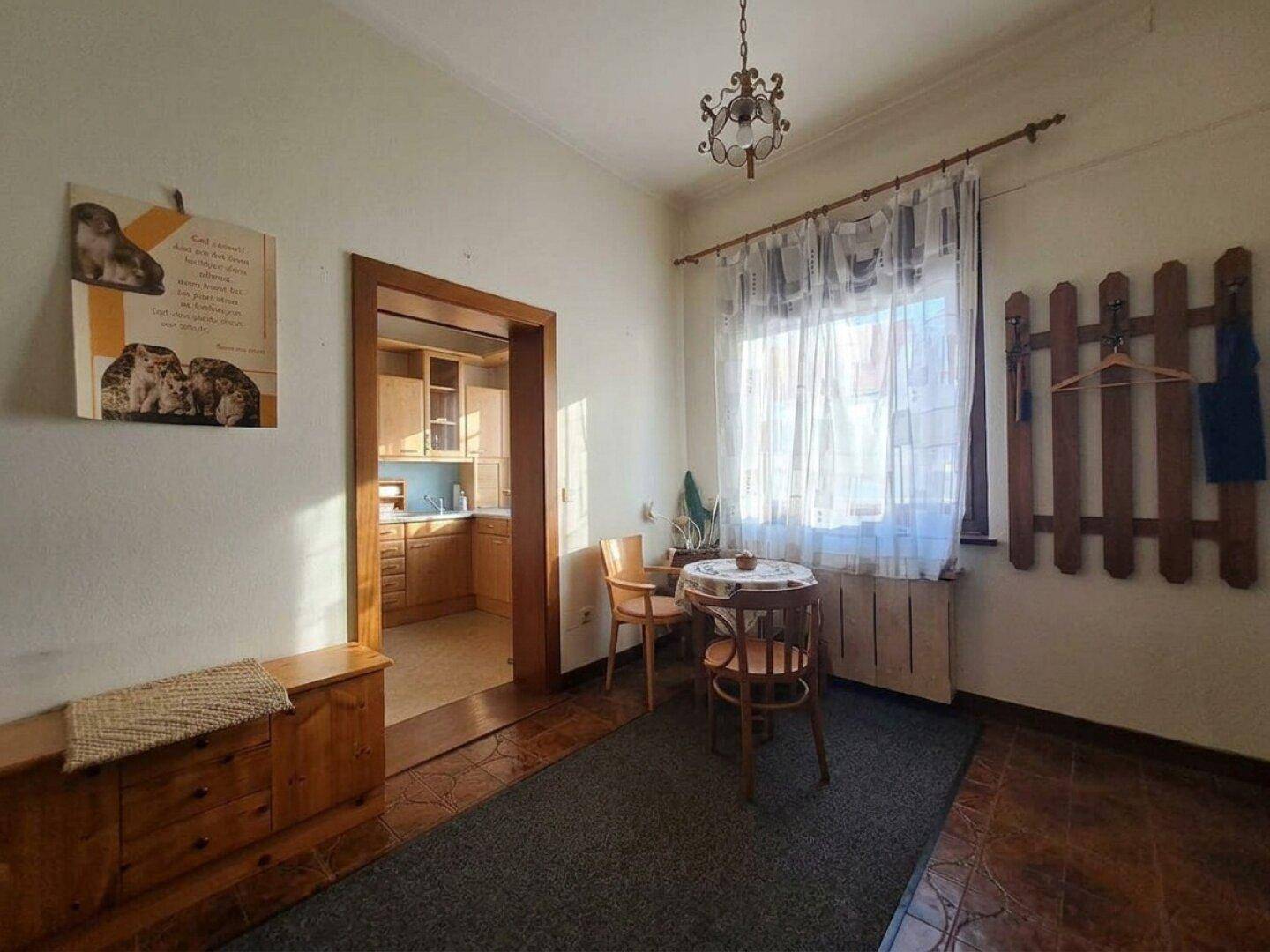 Gemütlicher Essbereich mit Fenster und Zugang zu einer Küche, ausgestattet mit traditionellen Möbeln.
