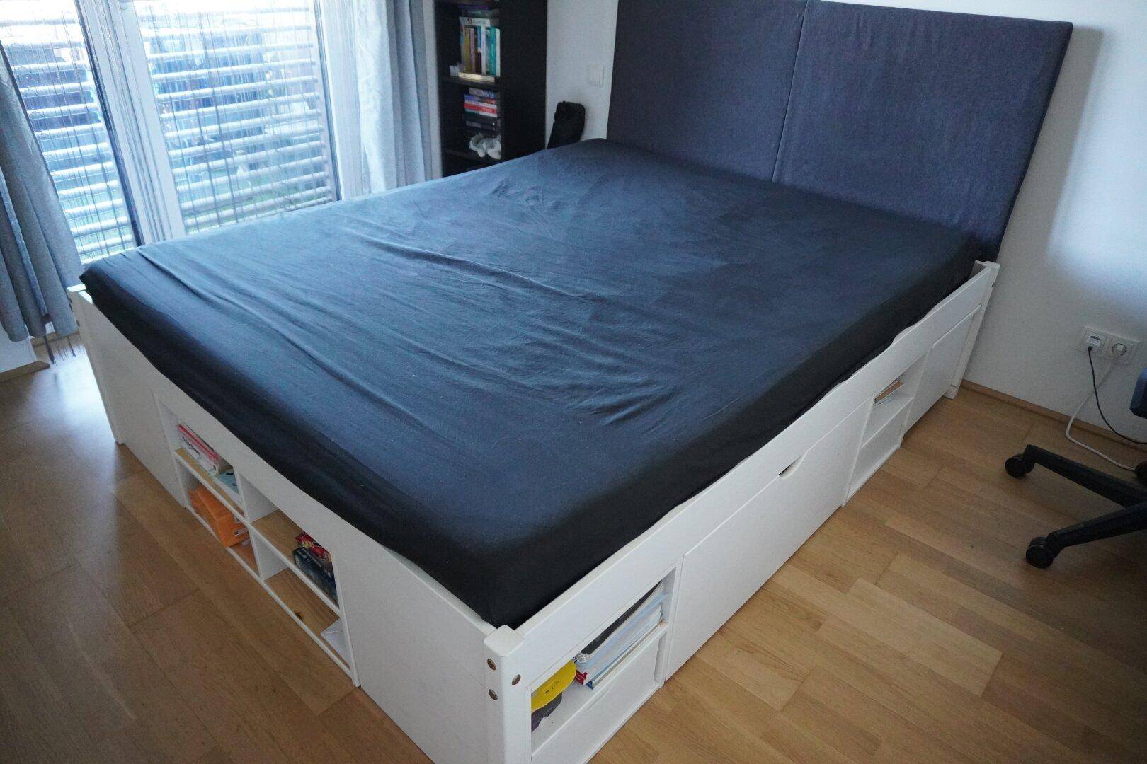 Schlafzimmer mit großem Bett und integriertem Stauraum, auf hellem Holzboden.