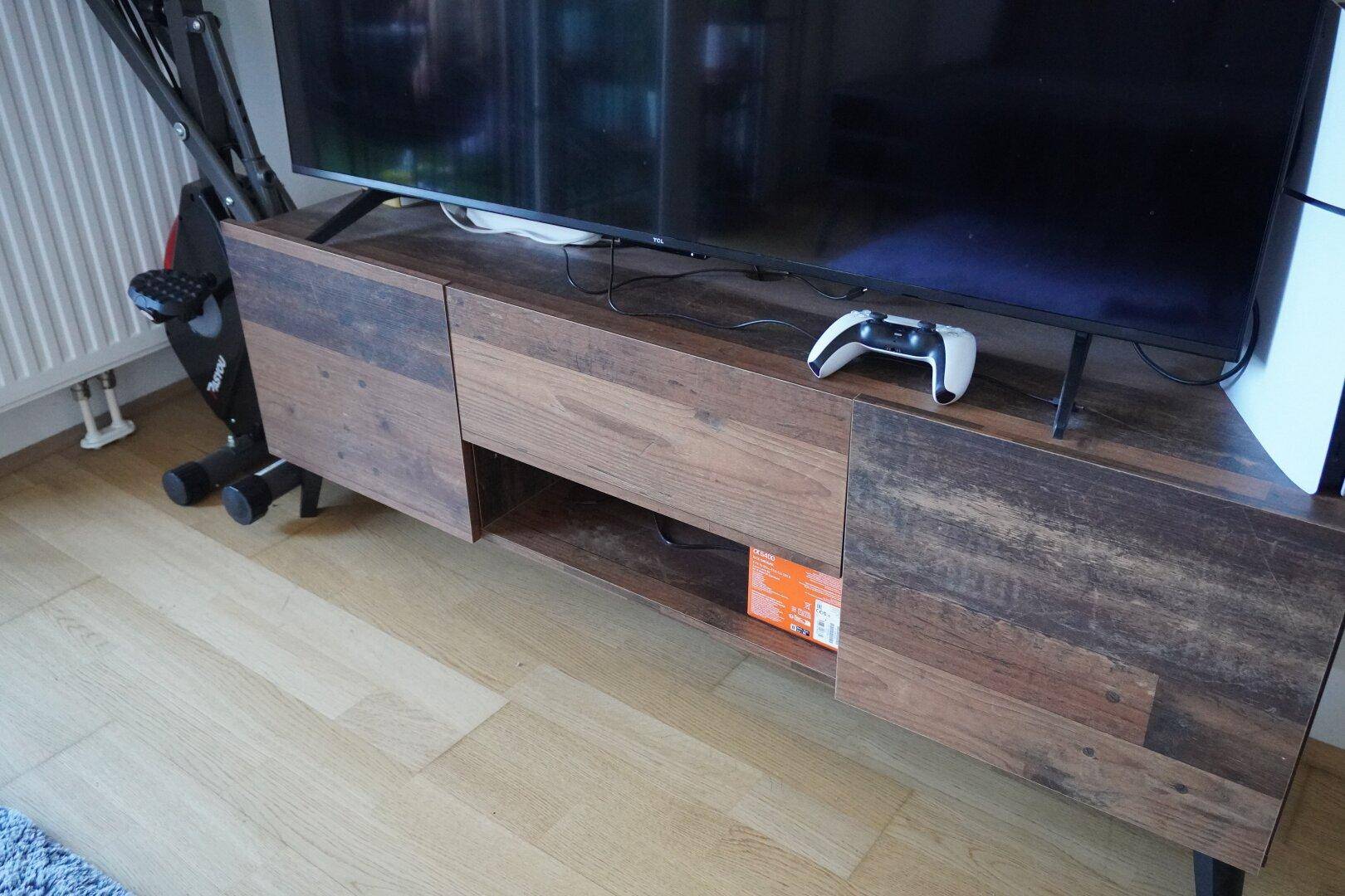Moderner TV-Schrank aus Holz mit Fernseher und Spielekonsole auf Holzboden.