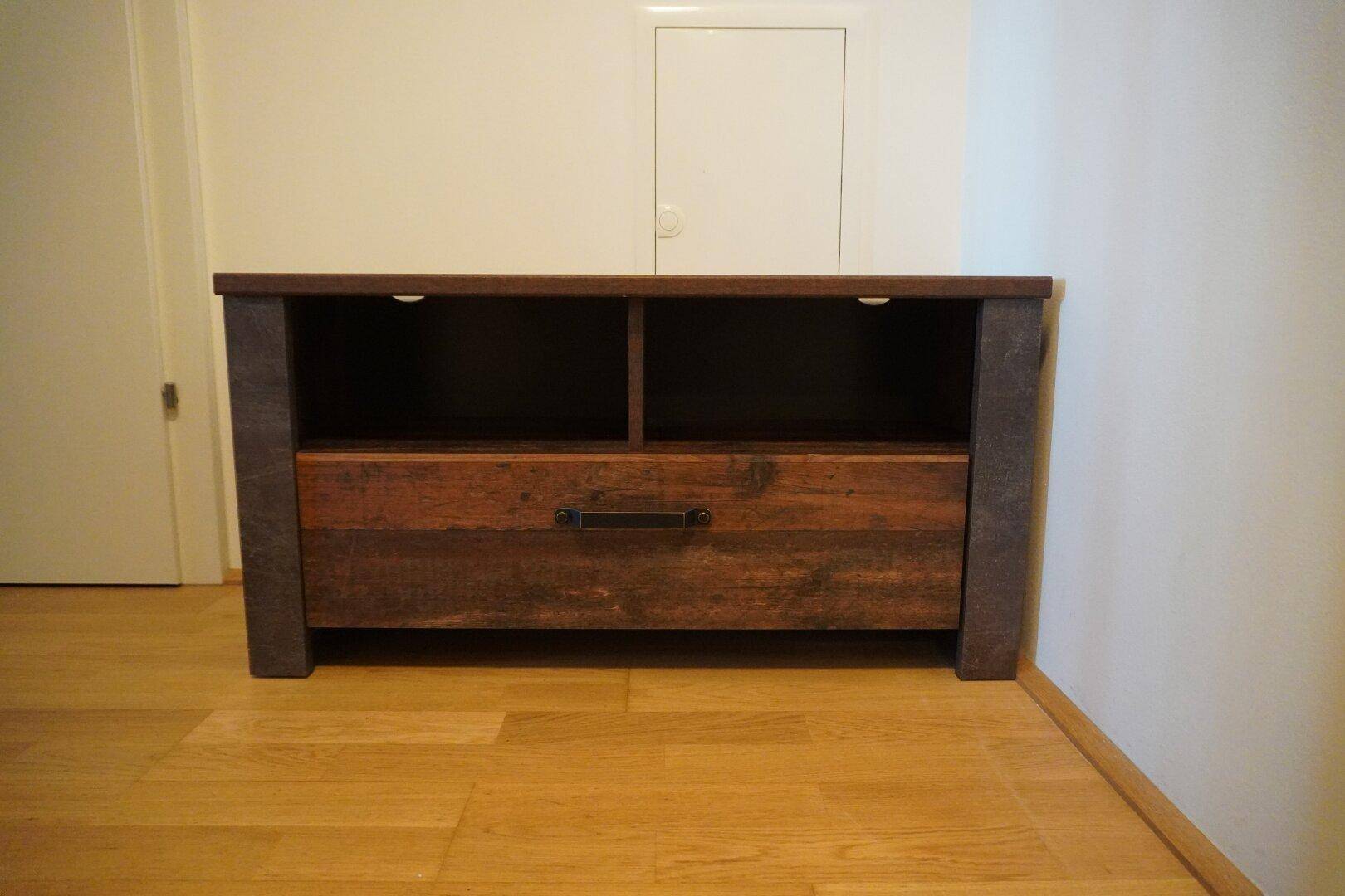 Niedriger Holzschrank mit Schublade und offenen Fächern, auf hellem Holzboden.
