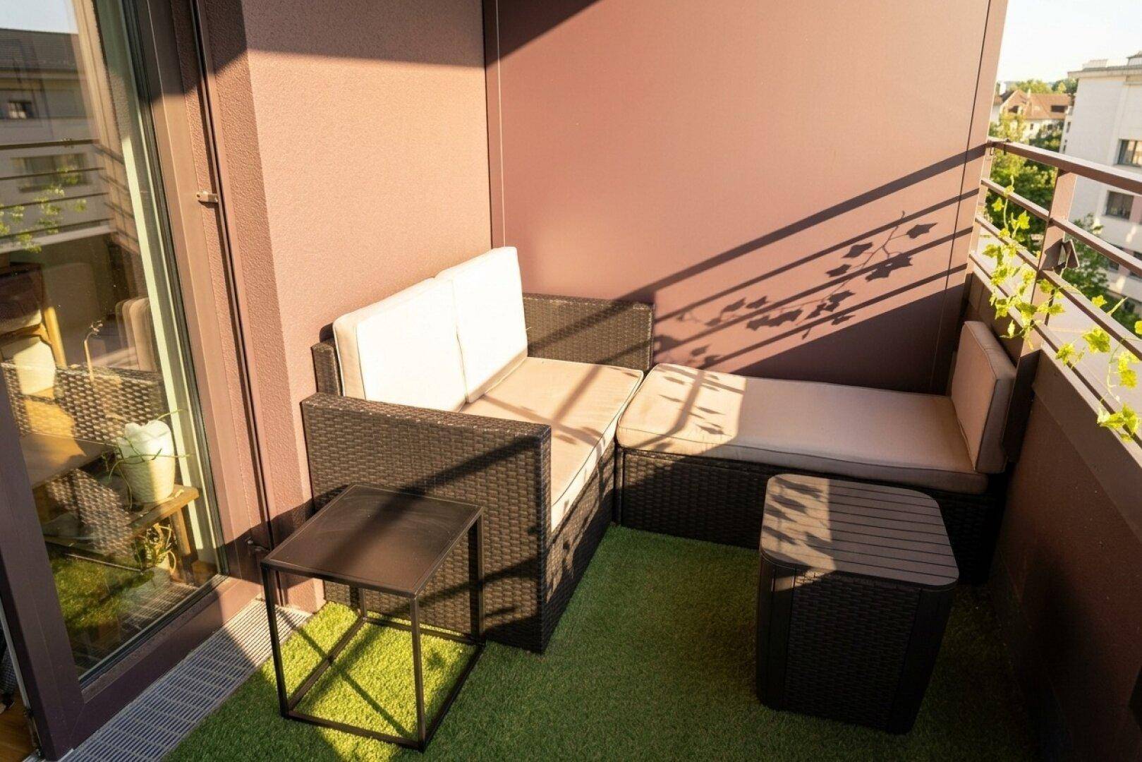 Gemütlicher Balkon mit Rattanmöbeln und Kunstrasen, ideal zum Entspannen in der Sonne.