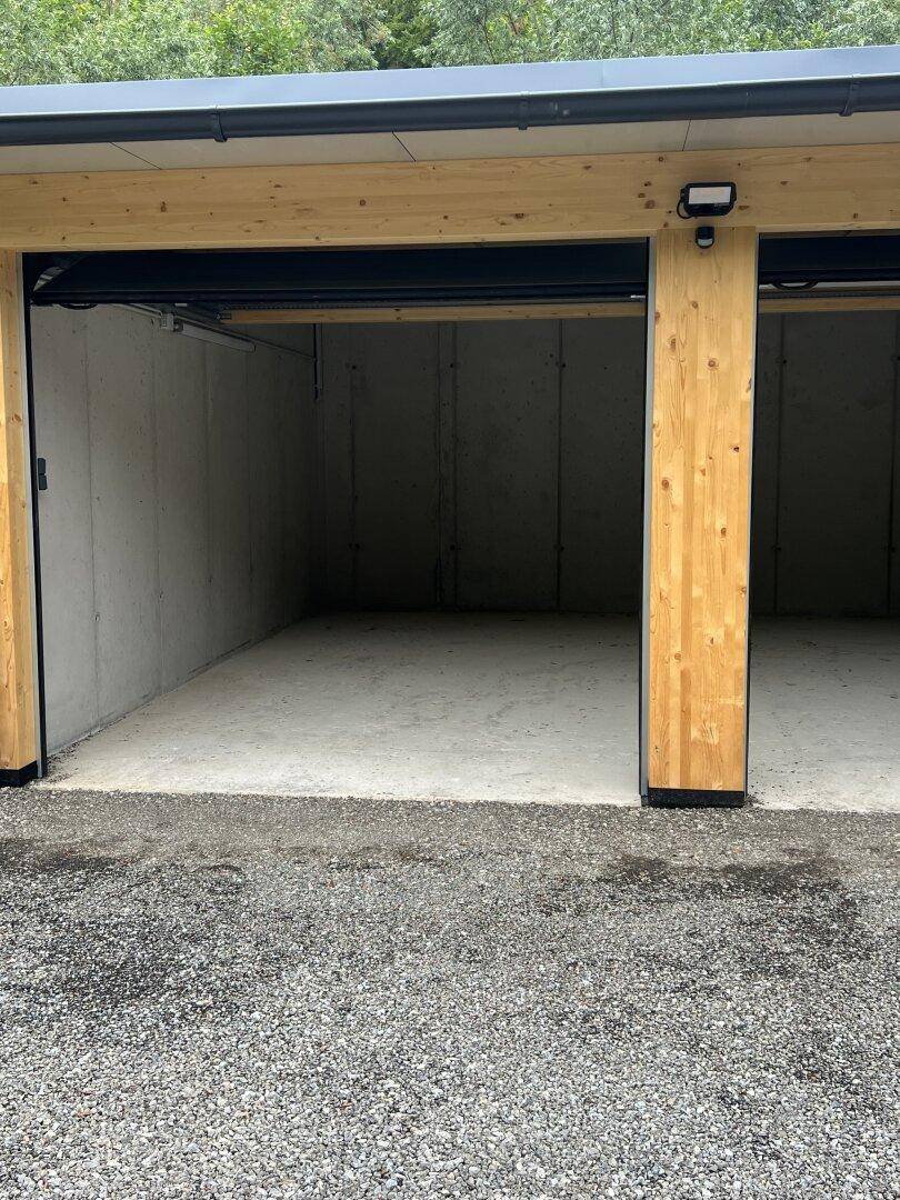 Eingang einer modernen Doppelgarage mit Holzbalken, Betonwänden und Schotterzufahrt.