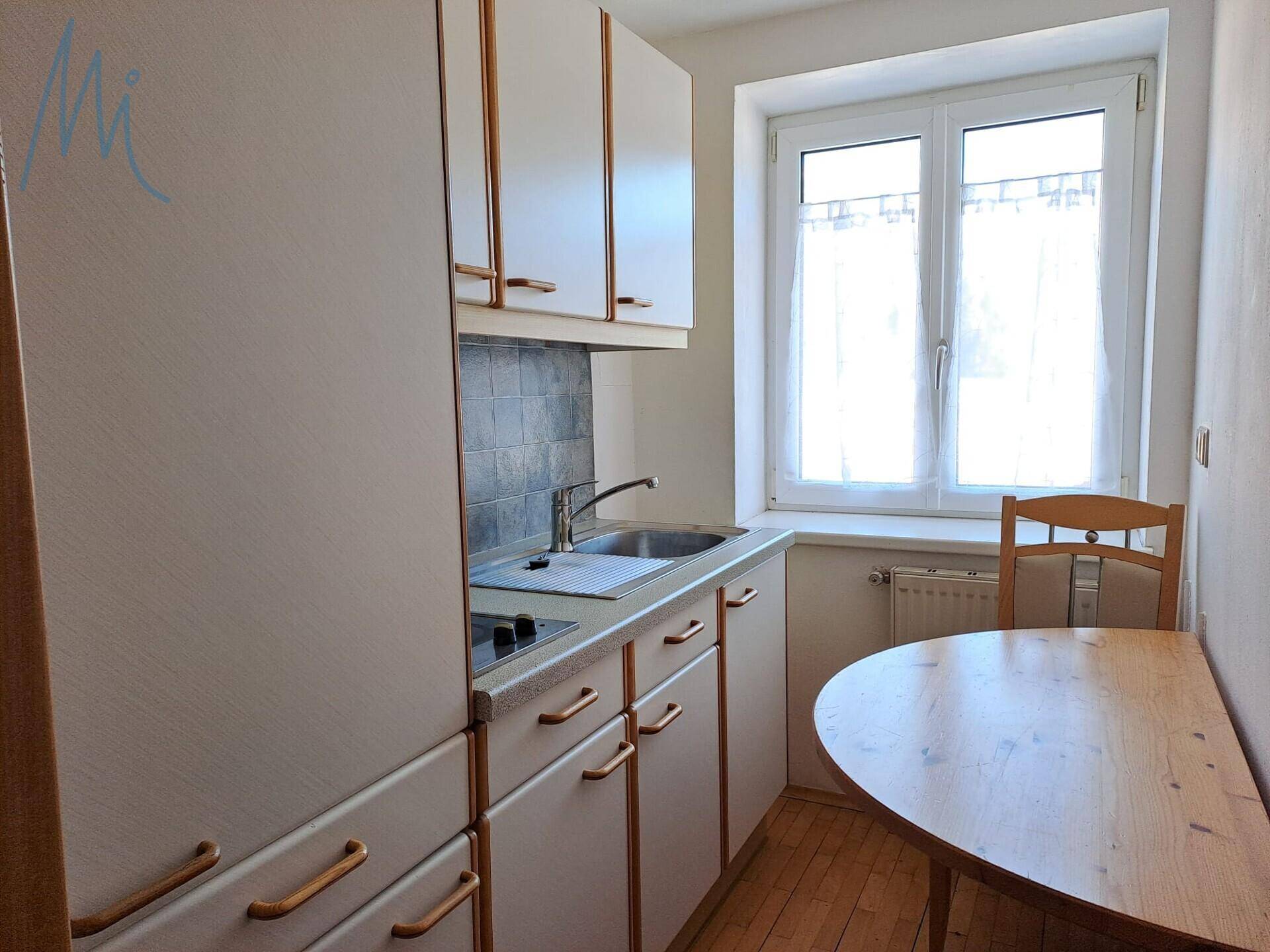 Kleine Küchenzeile mit Spüle, Kochfeld und Esstisch am Fenster.