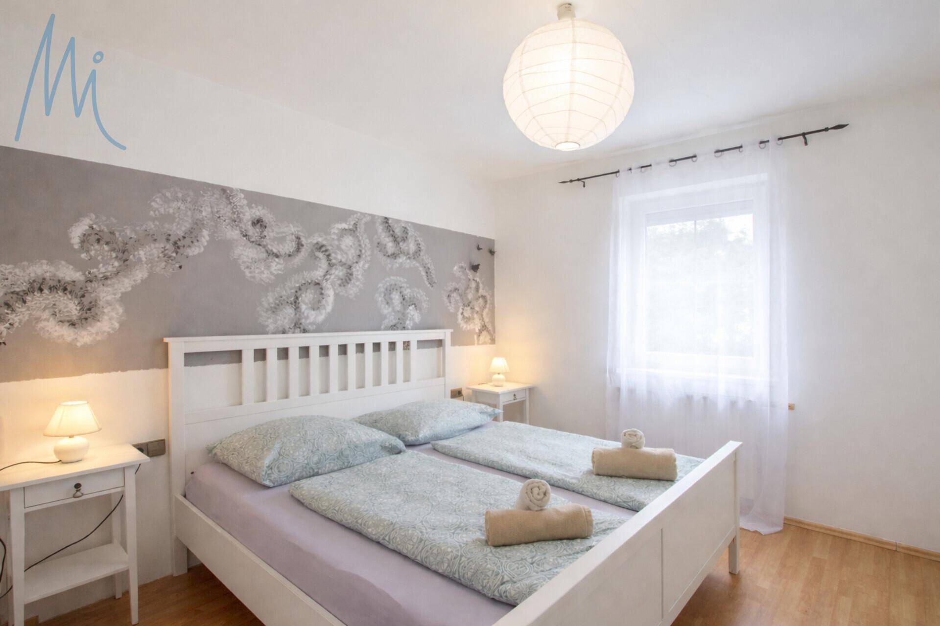 Helles Schlafzimmer mit Doppelbett, Holzboden und dekorativer Wandgestaltung.