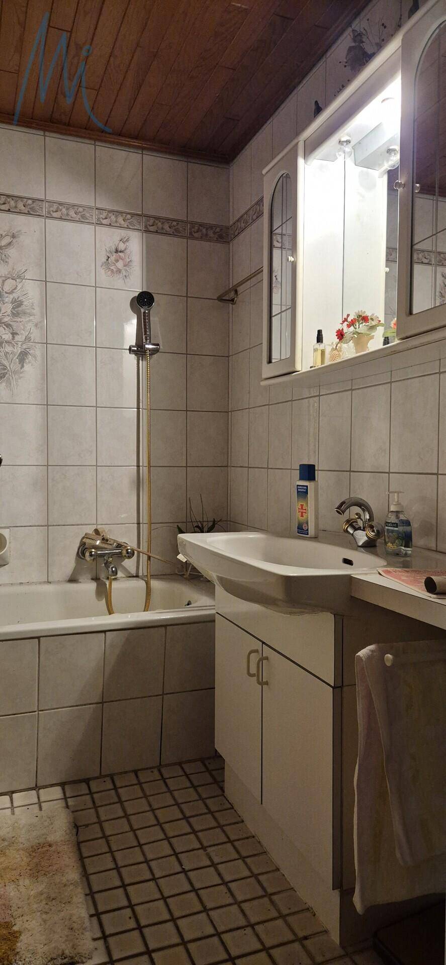 Badezimmer mit Waschbecken, Spiegelschrank, Badewanne mit Dusche und gefliesten Wänden.
