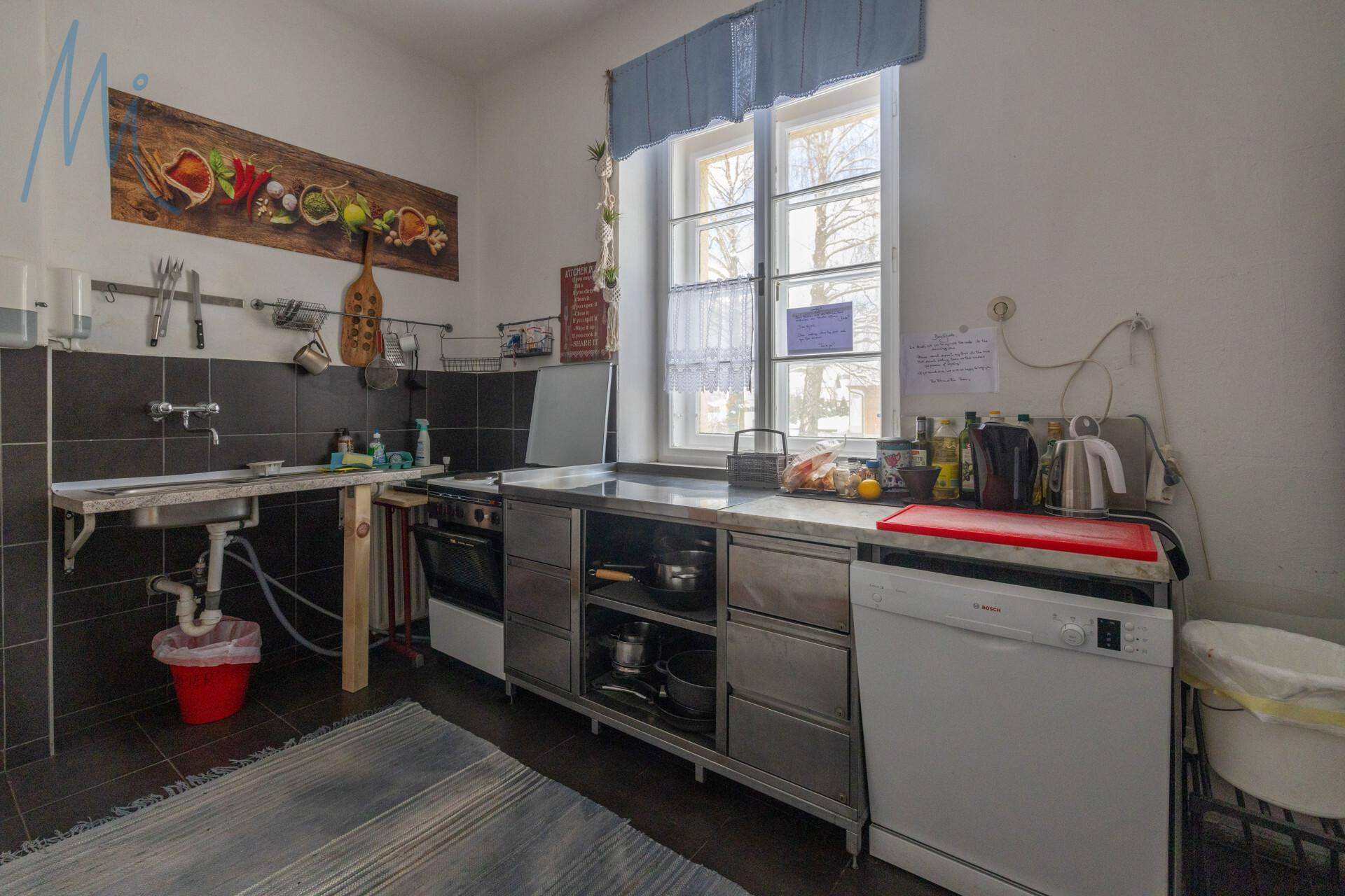 Funktionale Küche mit Edelstahlmöbeln, Spülmaschine und großem Fenster, ideal für die Zubereitung von Speisen.