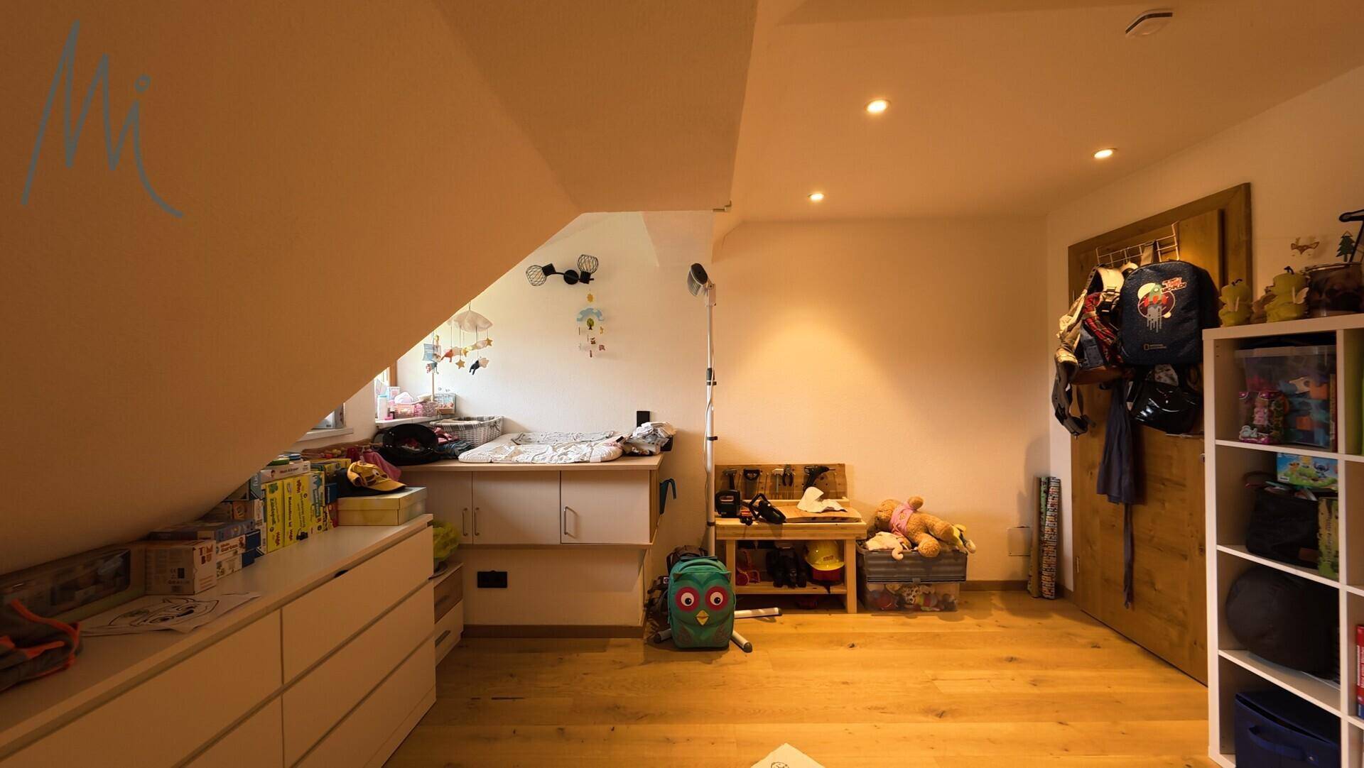 Kinderzimmer im Dachgeschoss mit schräger Decke, Holzboden und einem Fenster für Tageslicht.