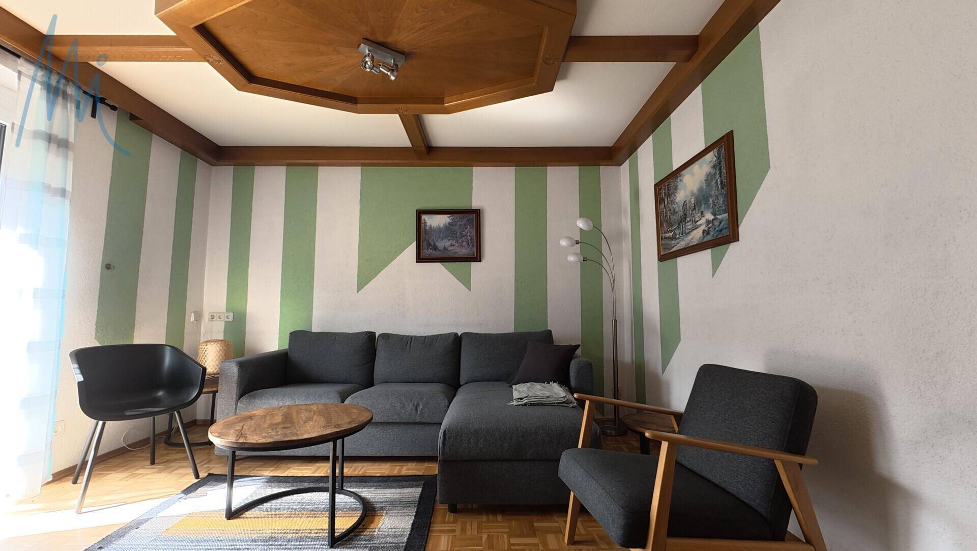 Wohnzimmer mit grünen Streifenwänden, Holzbalkendecke und modernem Sofa.