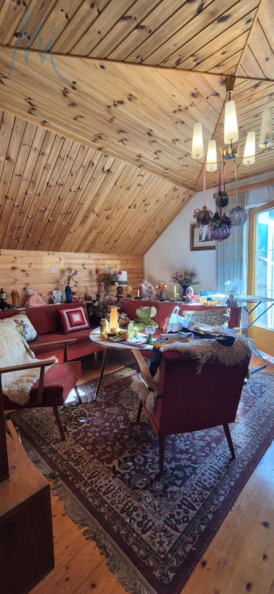 Gemütlicher Wohnbereich im Dachgeschoss mit Holzbalkendecke, Teppich und traditionellen Möbeln.