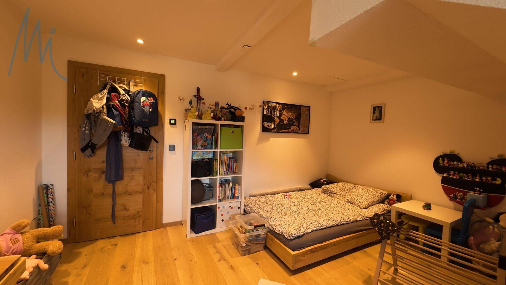 Gemütliches Schlafzimmer im Dachgeschoss mit Holzboden, schräger Decke und einem Bett.