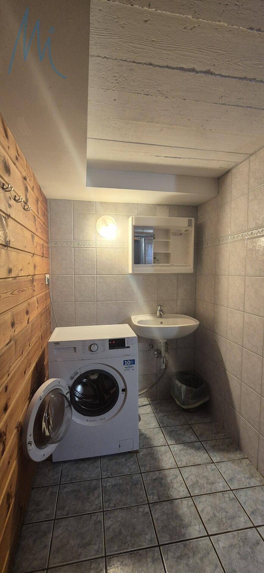 Praktischer Waschraum mit Waschmaschine, Waschbecken und Fliesenboden.