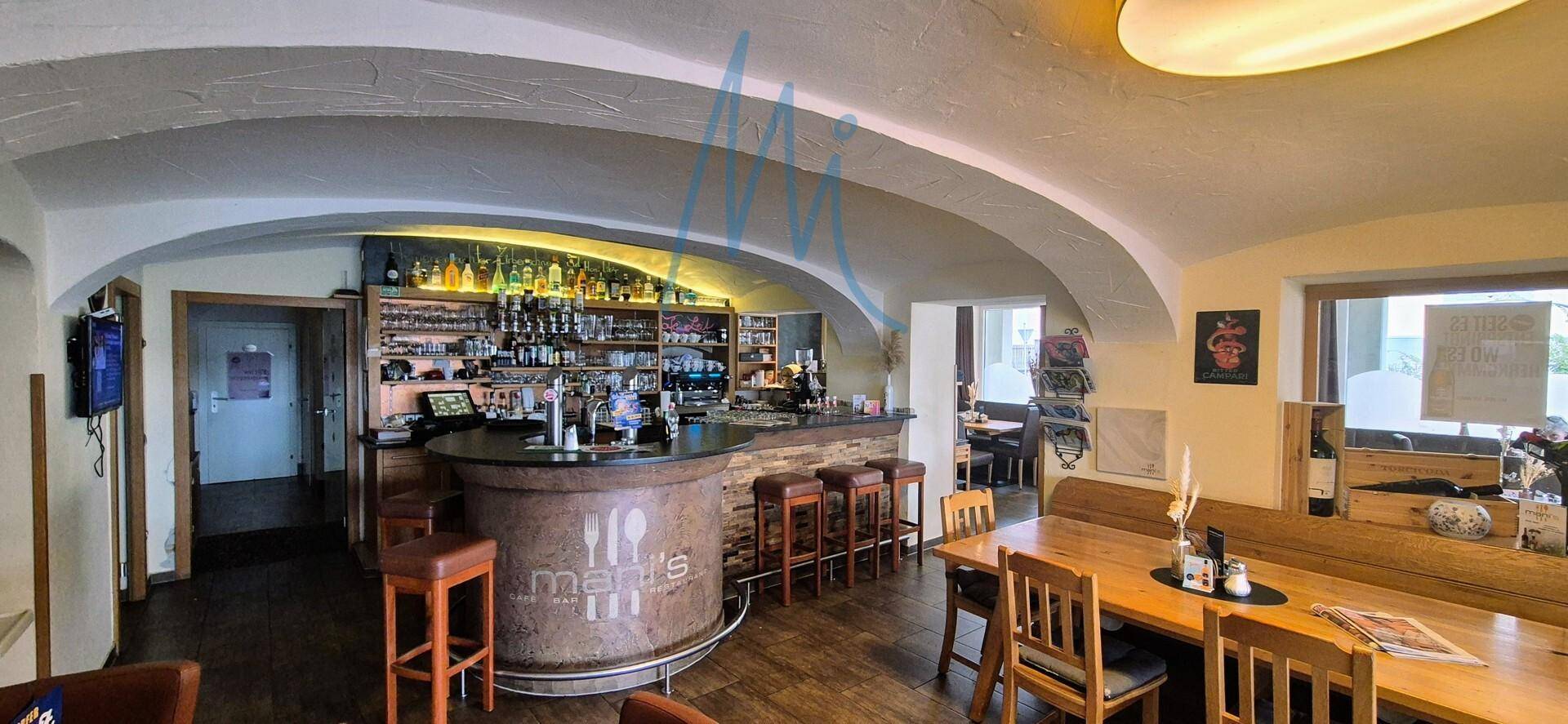 Gemütlicher Barbereich mit gut bestückter Theke, hohen Hockern und Holztischen unter gewölbter Decke.