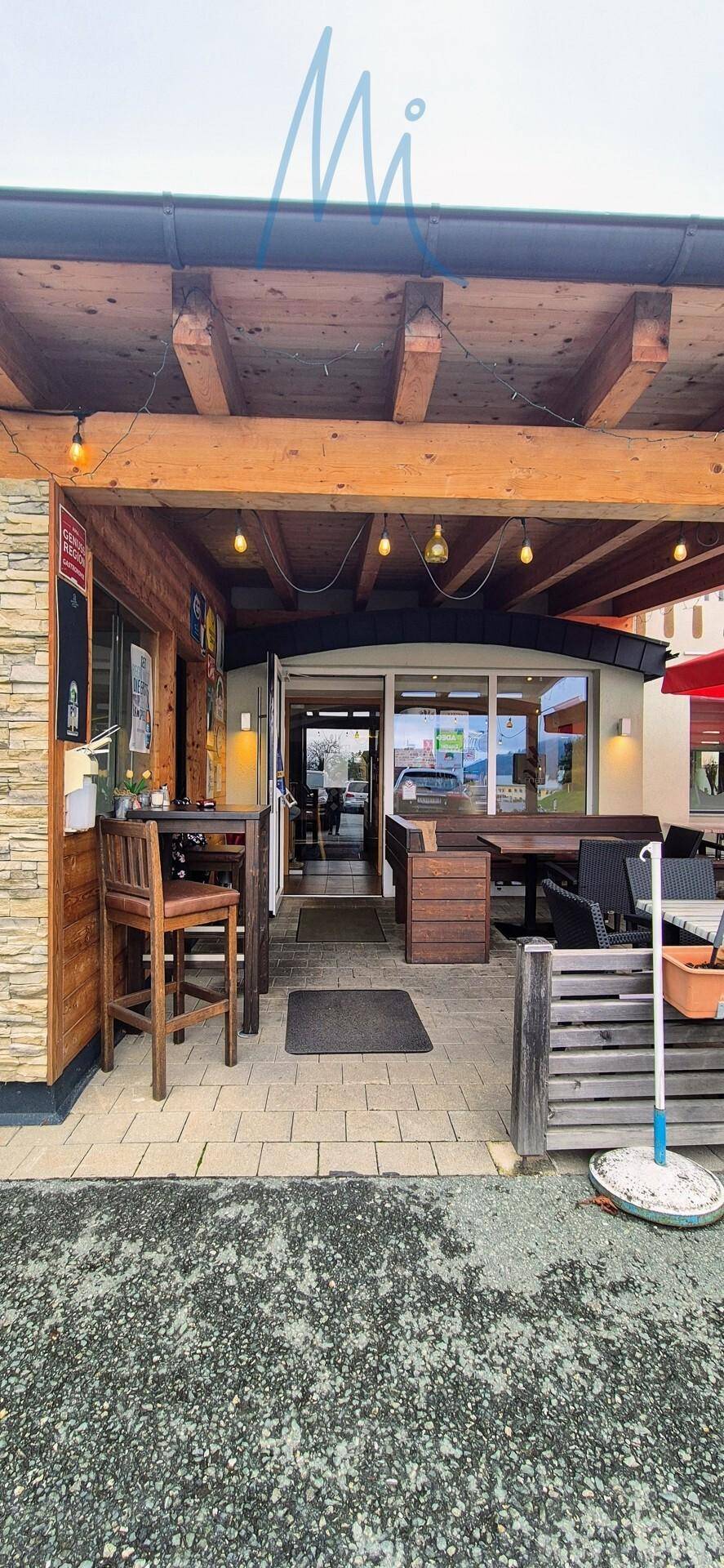 Eingangsbereich eines Restaurants mit überdachter Terrasse, Holzelementen und Außenbestuhlung.