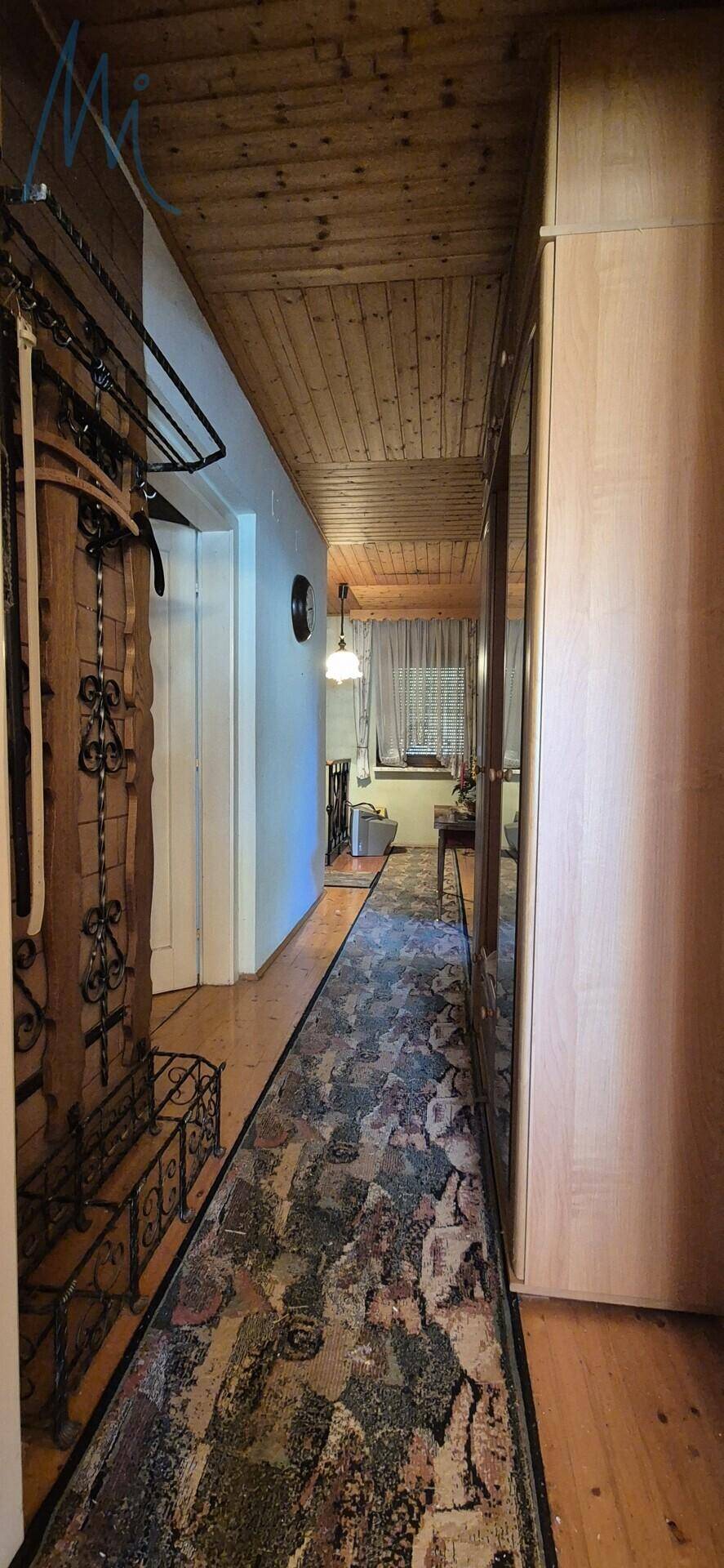 Flur mit Holzboden, schräger Holzdecke und einem langen Teppich, inklusive Einbauschrank.