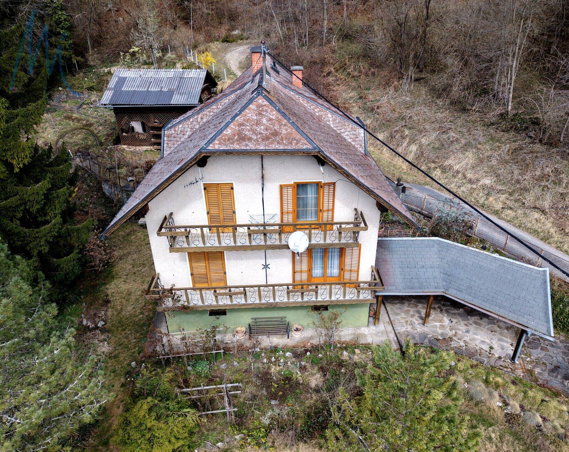 Traditionelles Haus mit mehreren Balkonen und Holzfensterläden, eingebettet in eine grüne Hügellandschaft.
