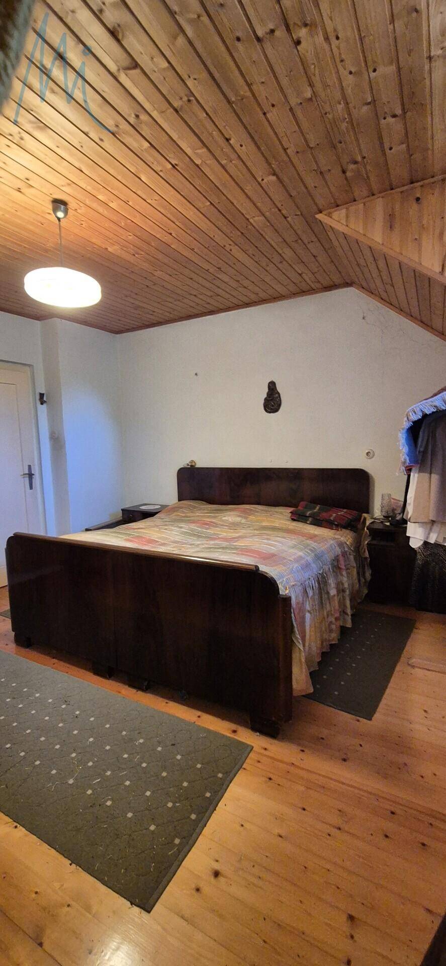 Weiterer Blick ins Schlafzimmer mit Holzbalkendecke, großem Bett und Teppich auf dem Holzboden.
