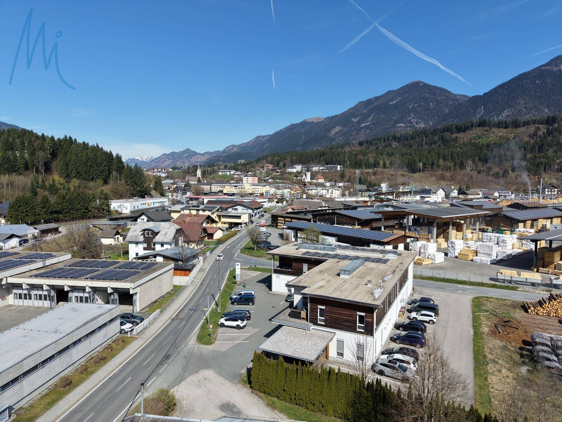 Panoramablick auf eine ländliche Ortschaft mit Bergen im Hintergrund und einigen Gebäuden mit Solaranlagen.