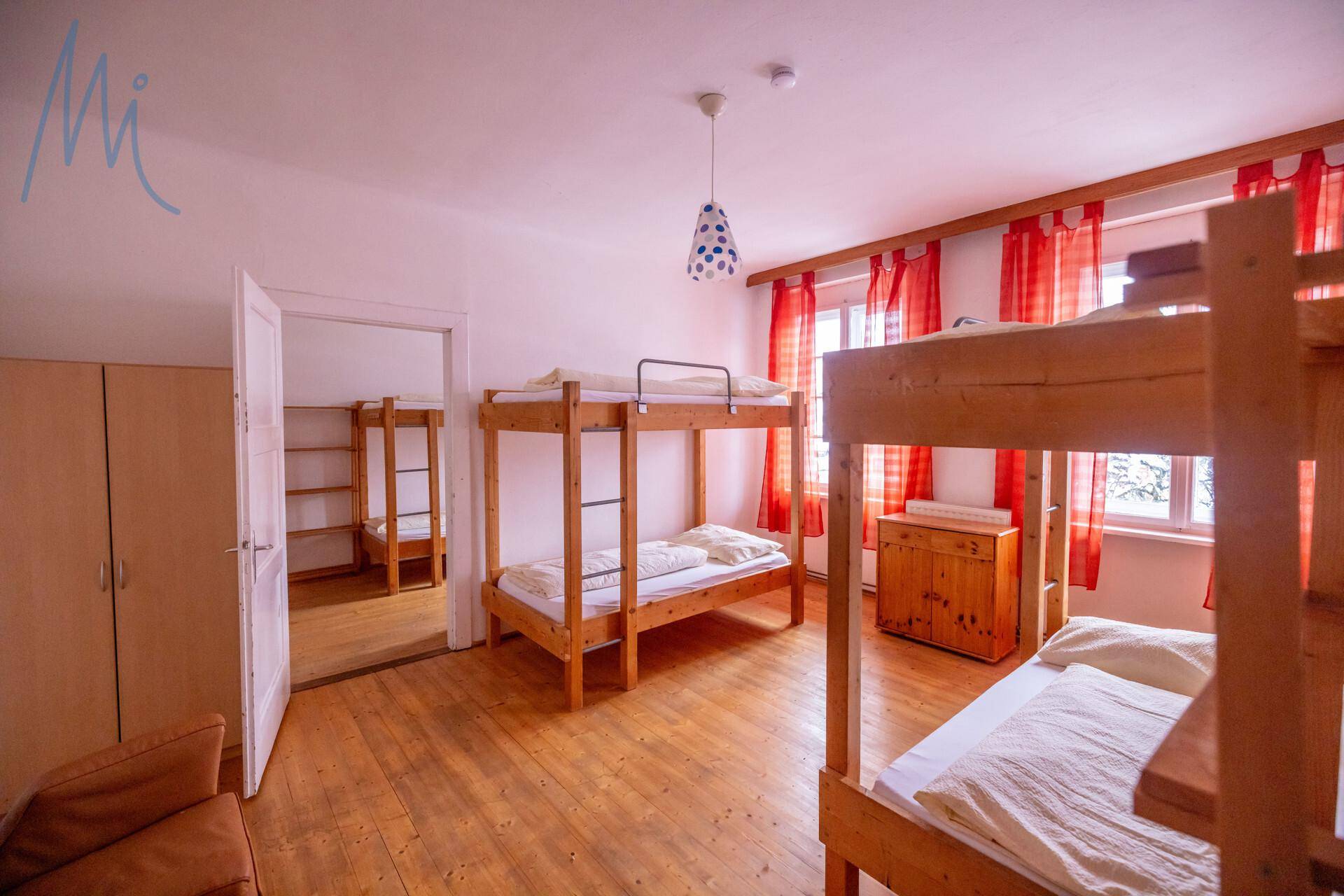 Geräumiges Schlafzimmer mit mehreren Etagenbetten und Holzboden, hell durch große Fenster.