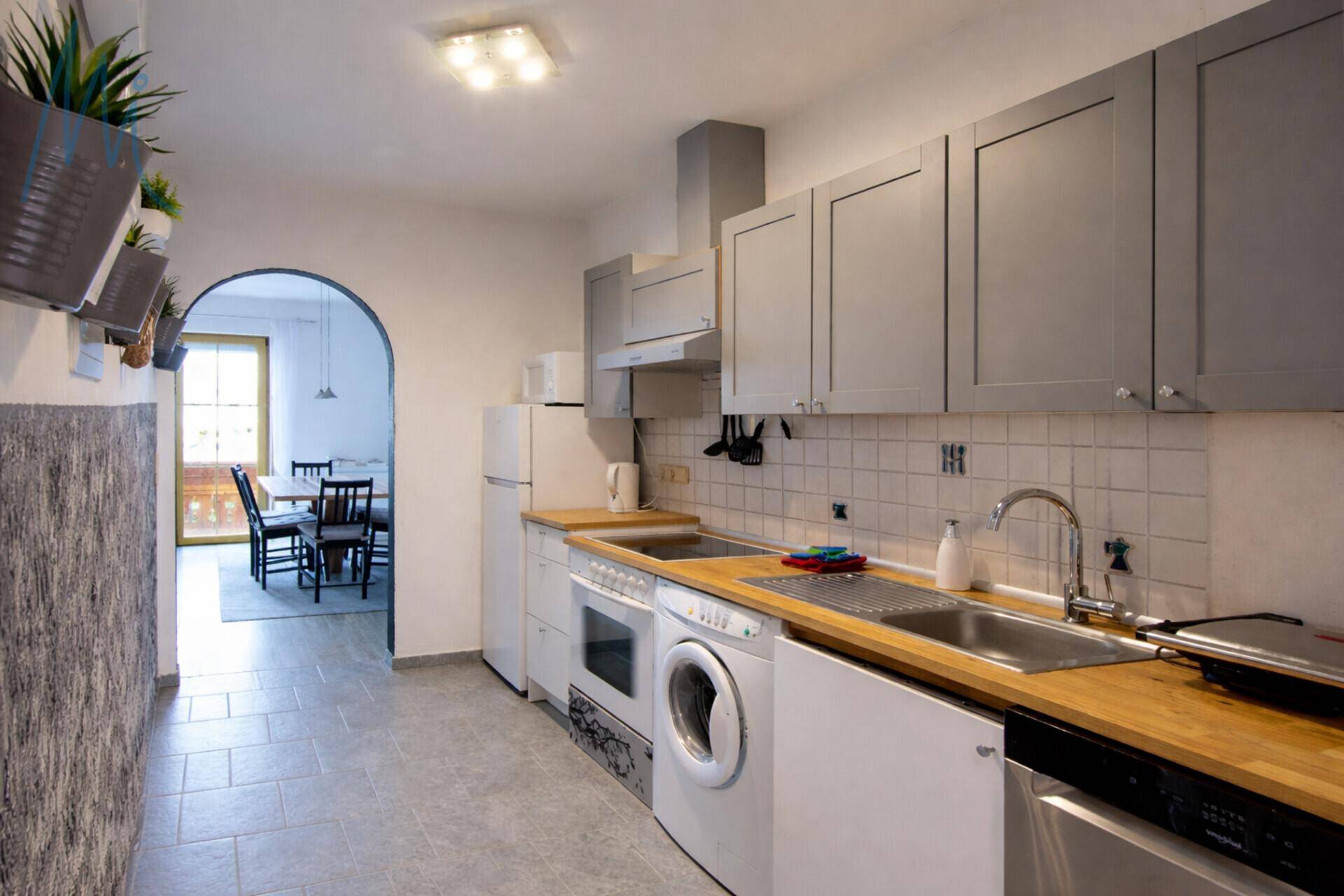 Funktionale Küche mit grauen Schränken, Holz-Arbeitsplatten und Fliesenboden.