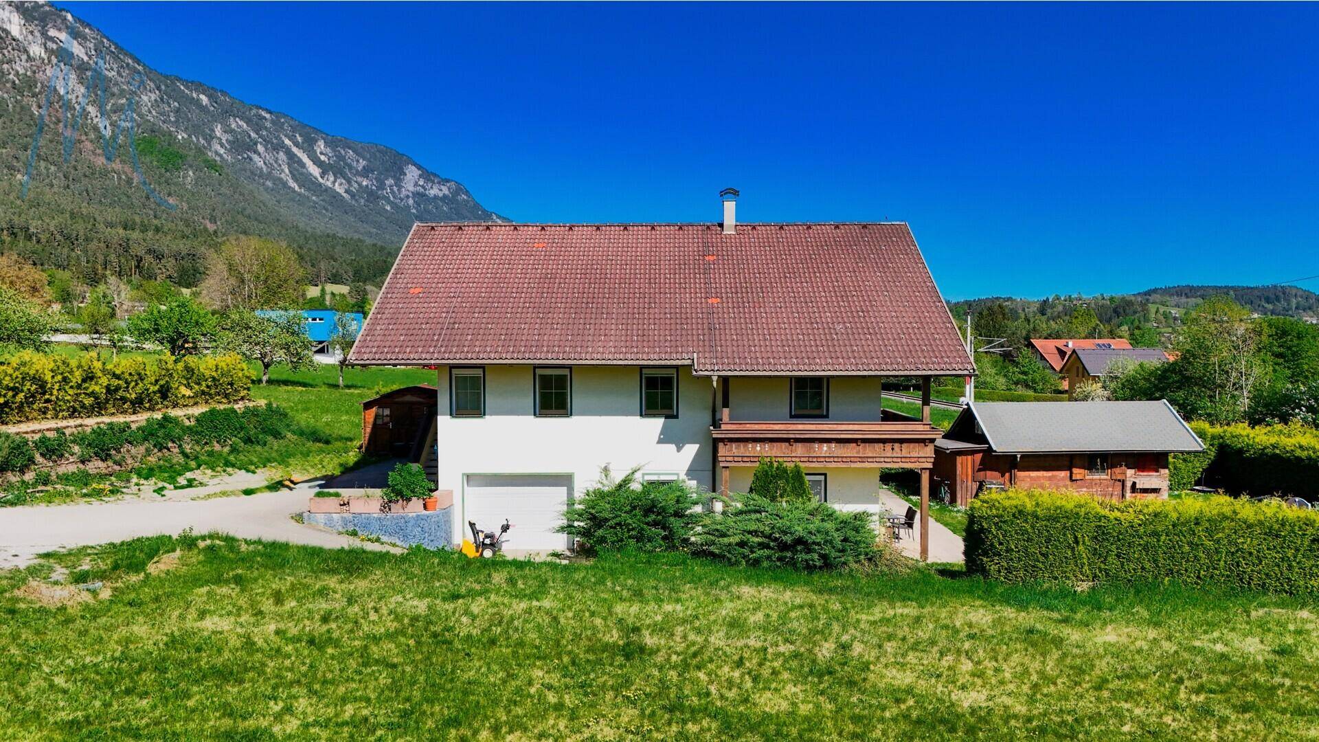 Seitenansicht des Hauses mit integrierter Garage, kleinem Balkon und weitem Blick auf die Berge.