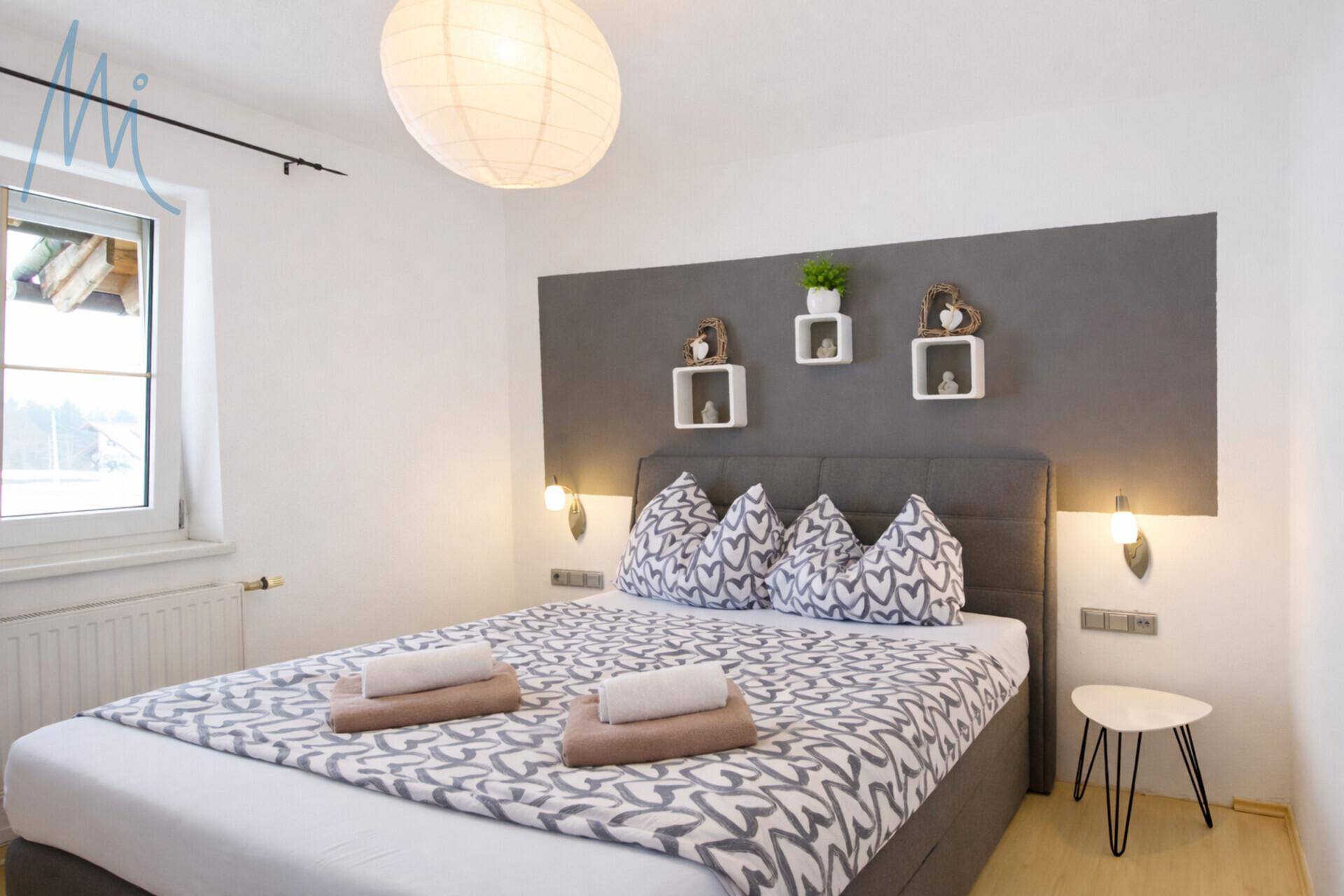 Modern eingerichtetes Schlafzimmer mit Doppelbett, grauer Akzentwand und Holzboden.