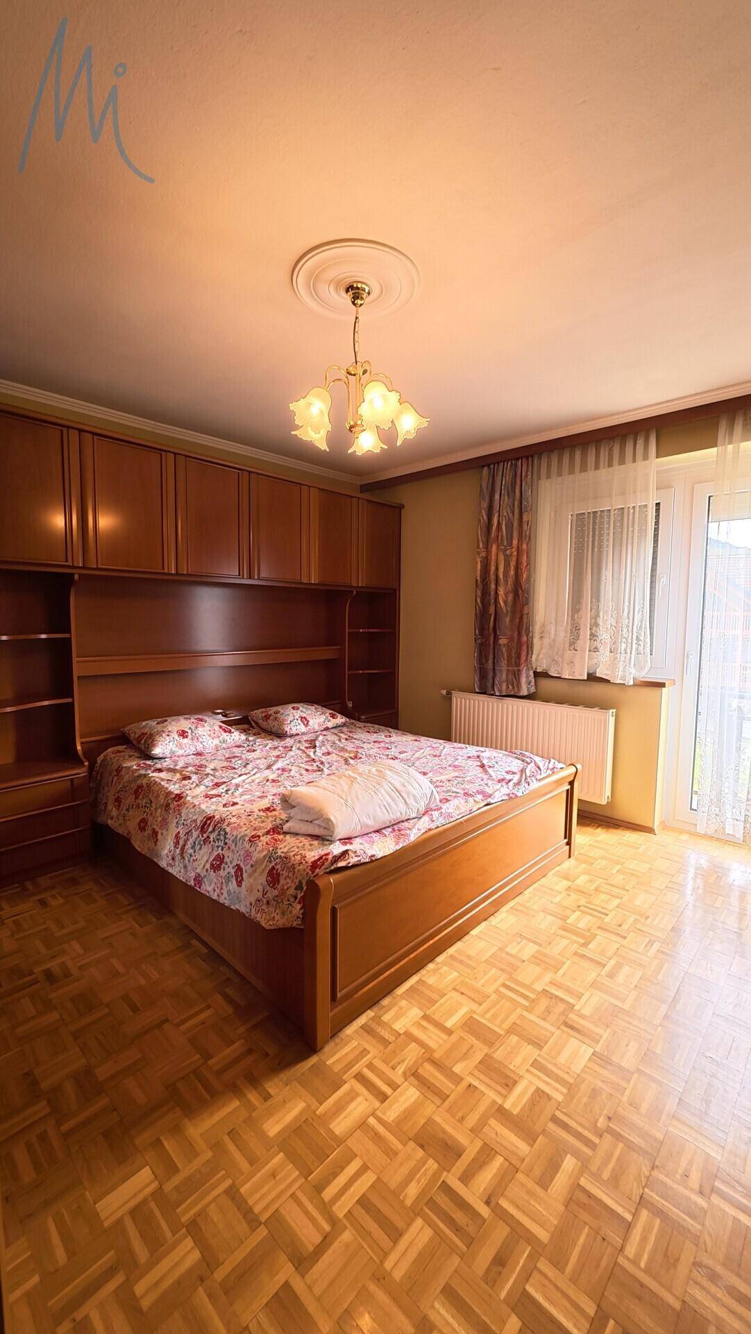 Schlafzimmer mit Holzboden, Einbauschränken und Zugang zum Balkon.