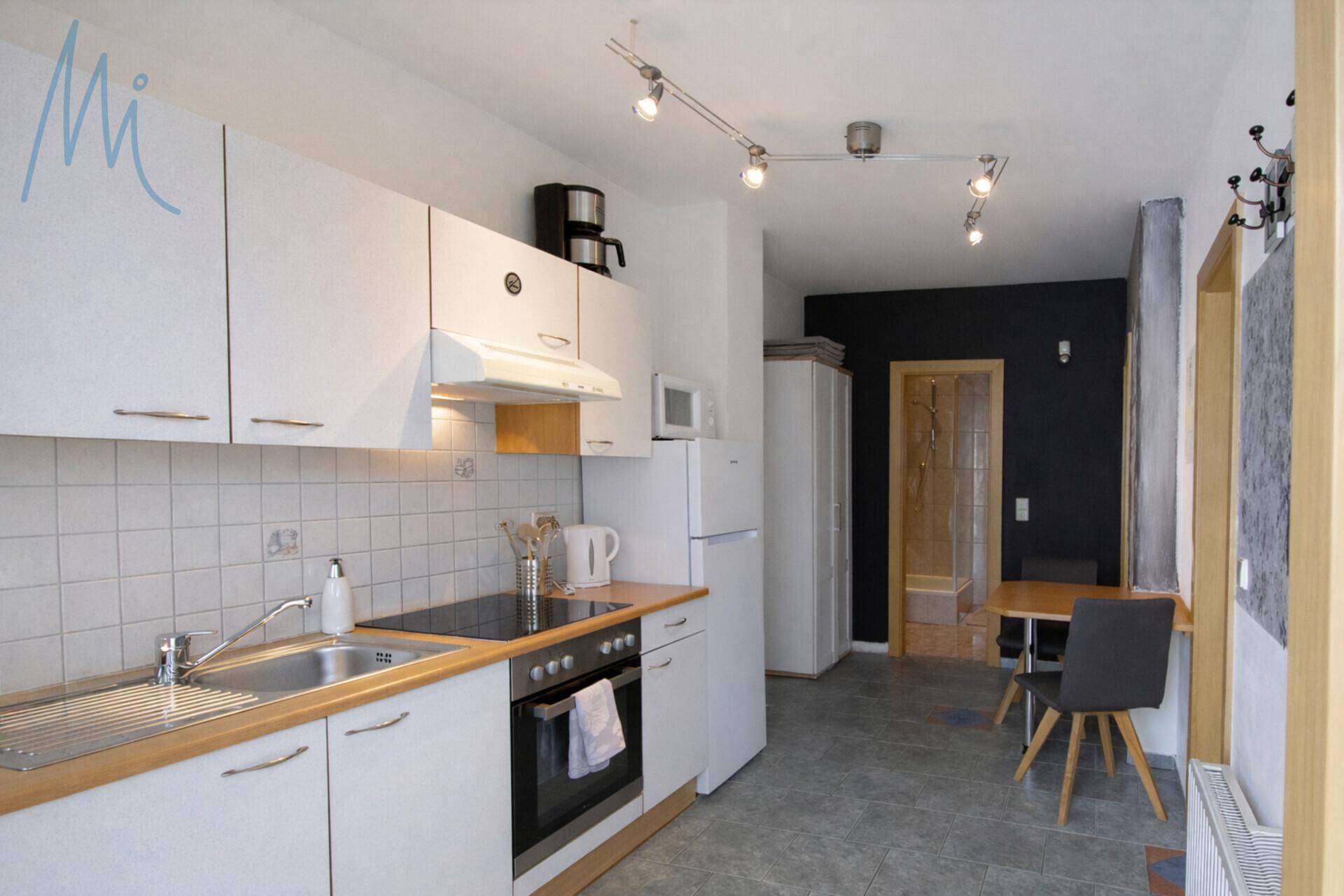 Funktionale weiße Küche mit Kochfeld, Backofen und Kühlschrank, ideal für Ferienwohnungen.