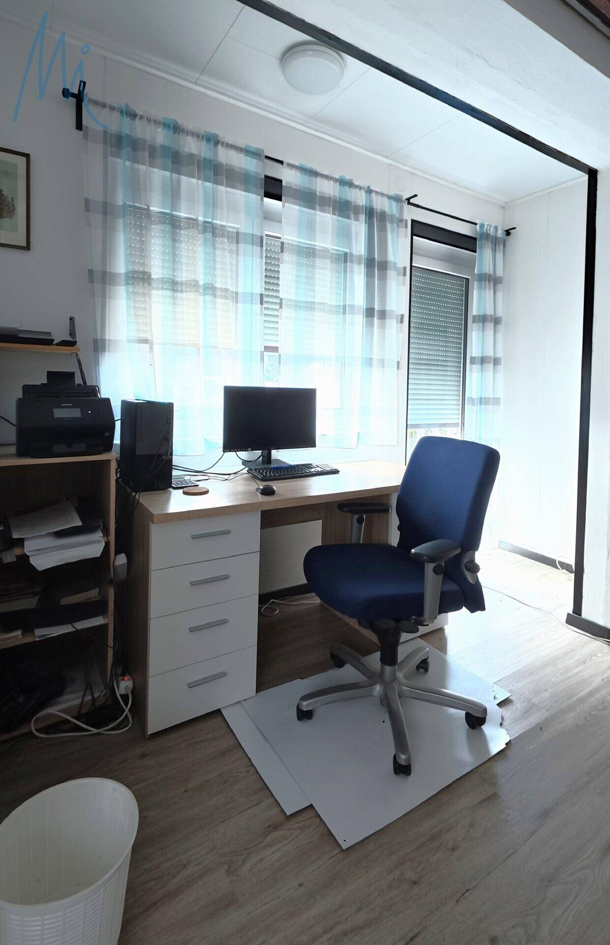 Helles Arbeitszimmer mit Schreibtisch, Bürostuhl und Fenster mit Rollladen.
