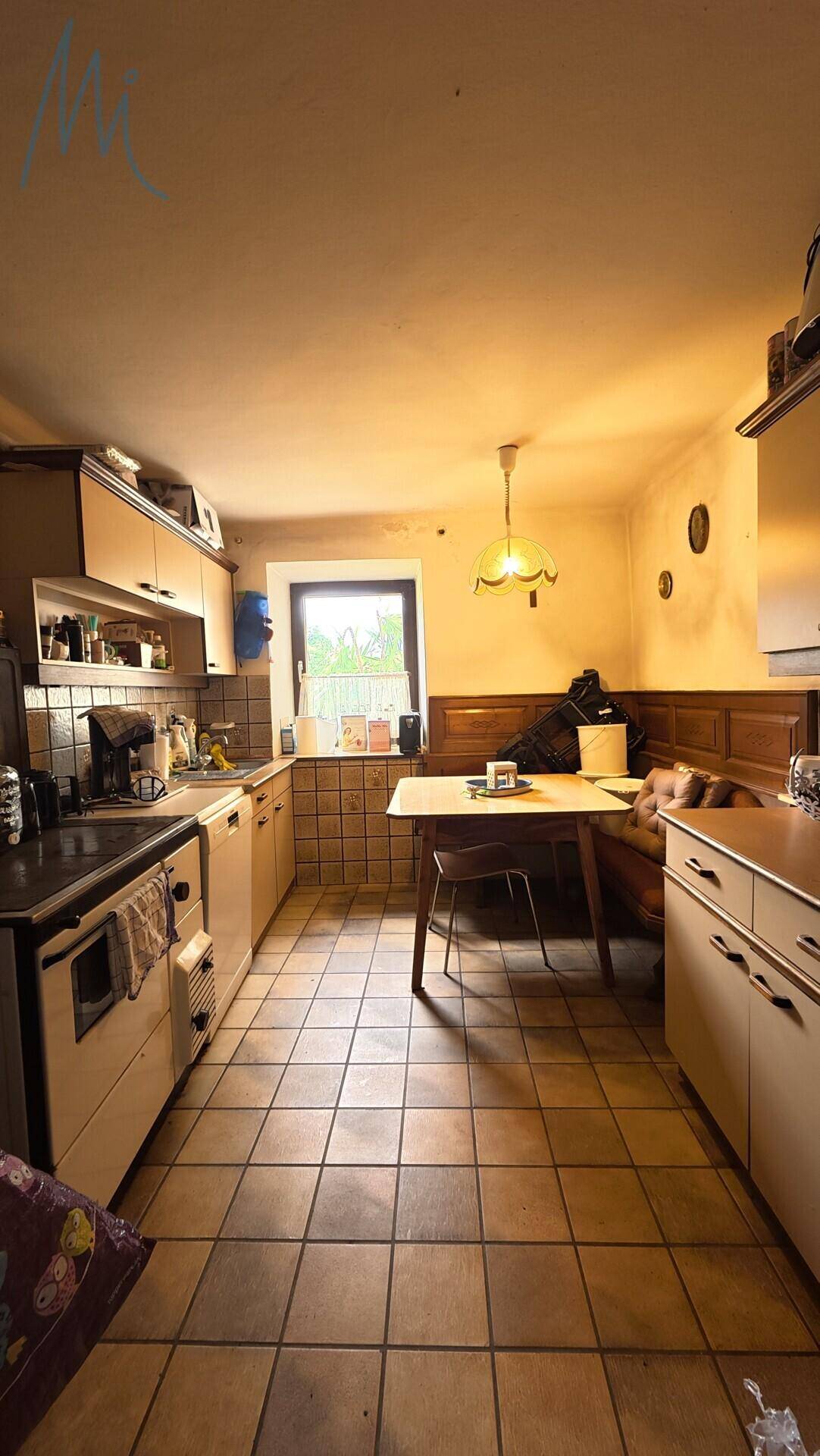 Traditionelle Küche mit Fliesenboden, Einbauschränken und einer gemütlichen Essecke am Fenster.