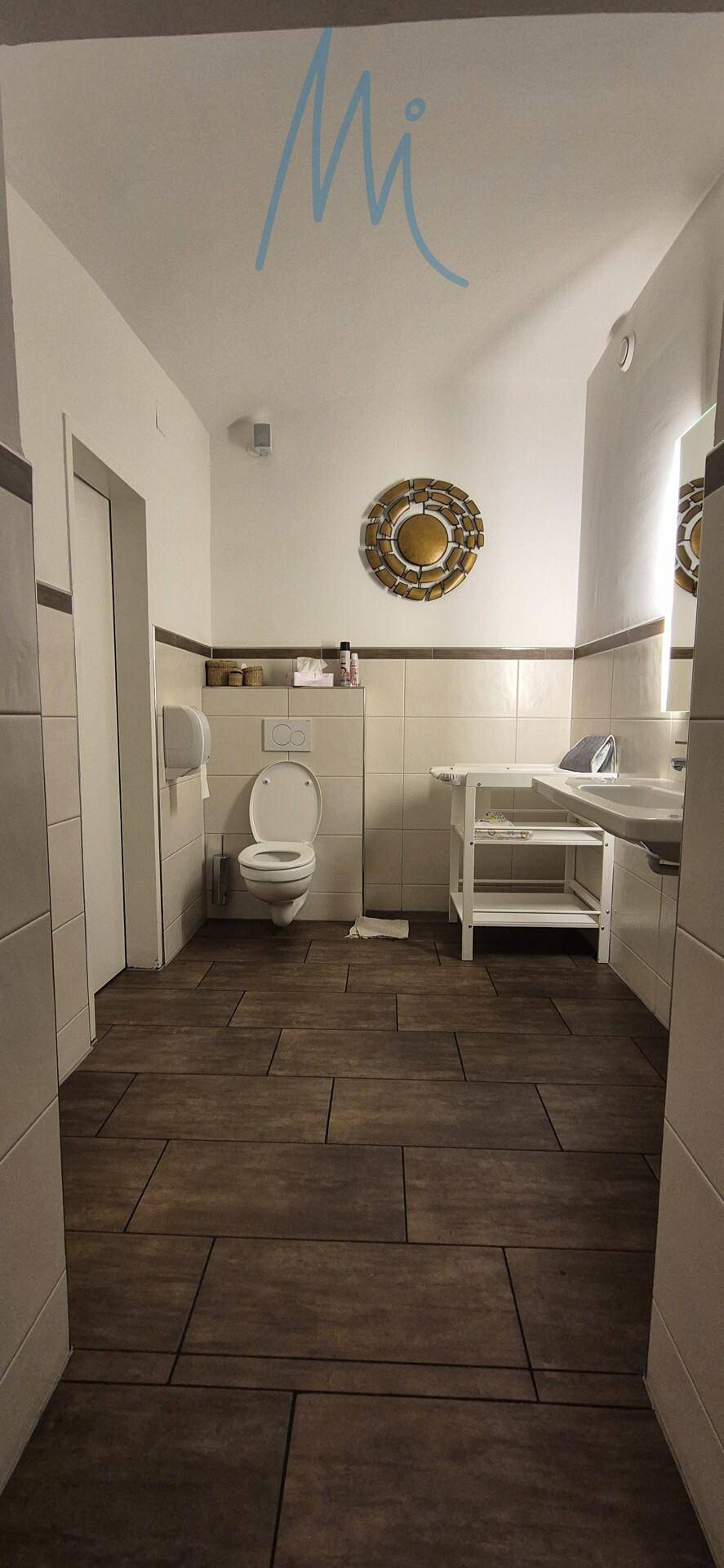 Sauberer Toilettenraum mit Fliesenboden, Wand-WC und Handwaschbecken, gut beleuchtet.