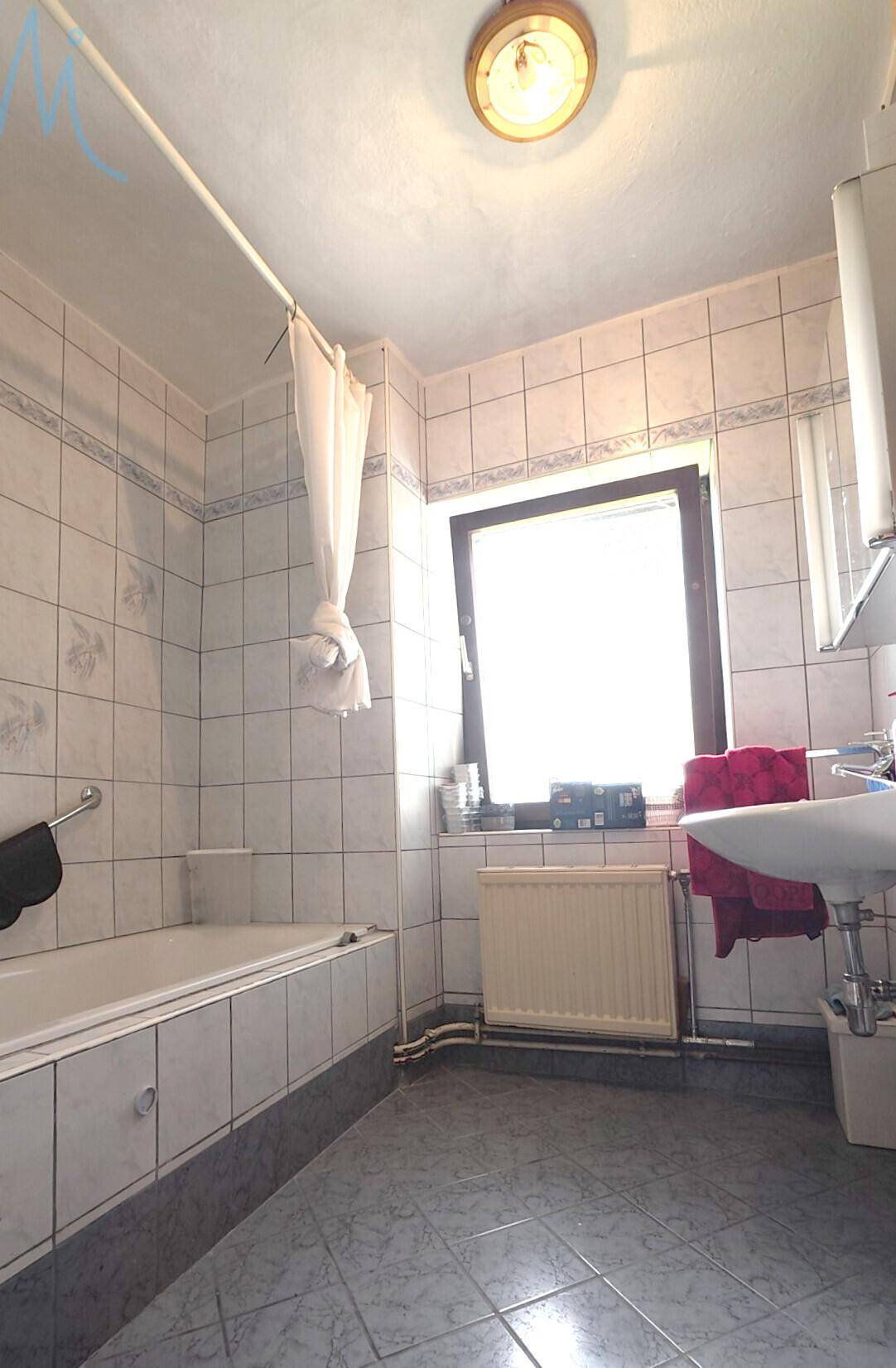 Gefliestes Badezimmer mit Badewanne, Waschbecken und Fenster für natürliche Belüftung.