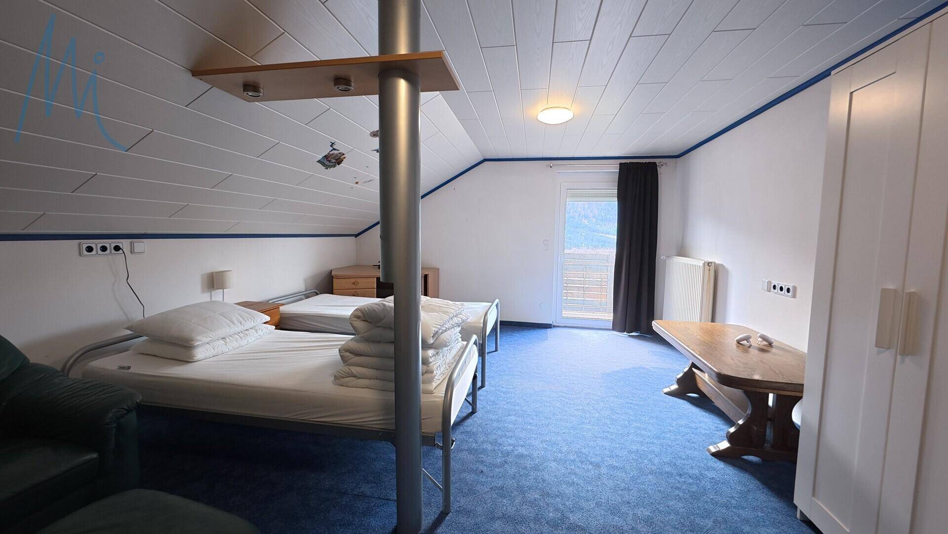 Geräumiges Dachgeschoss-Schlafzimmer mit zwei Einzelbetten und blauem Teppichboden.