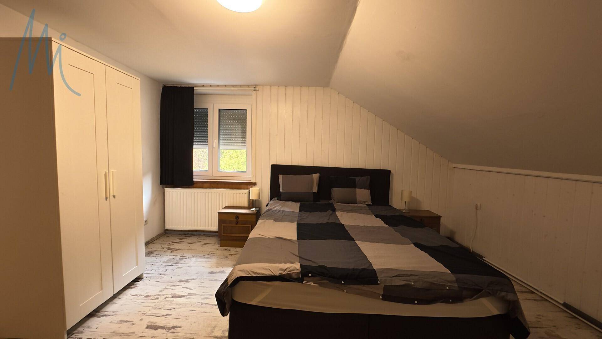 Dachgeschoss-Schlafzimmer mit schrägen Wänden, Doppelbett und Kleiderschrank.