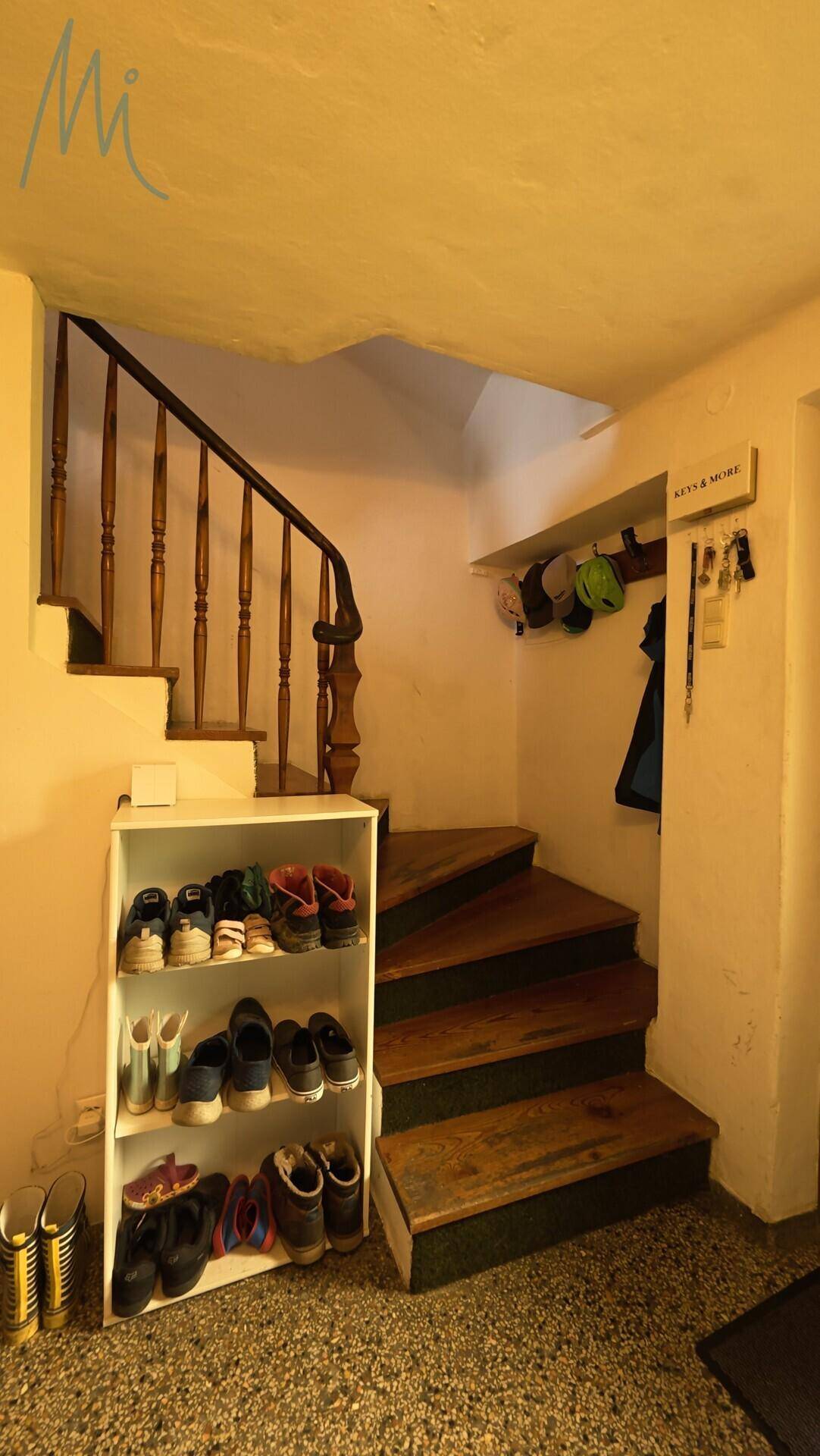 Treppenhaus mit Holzgeländer und einem Schuhregal, das den Zugang zu den oberen Etagen ermöglicht.