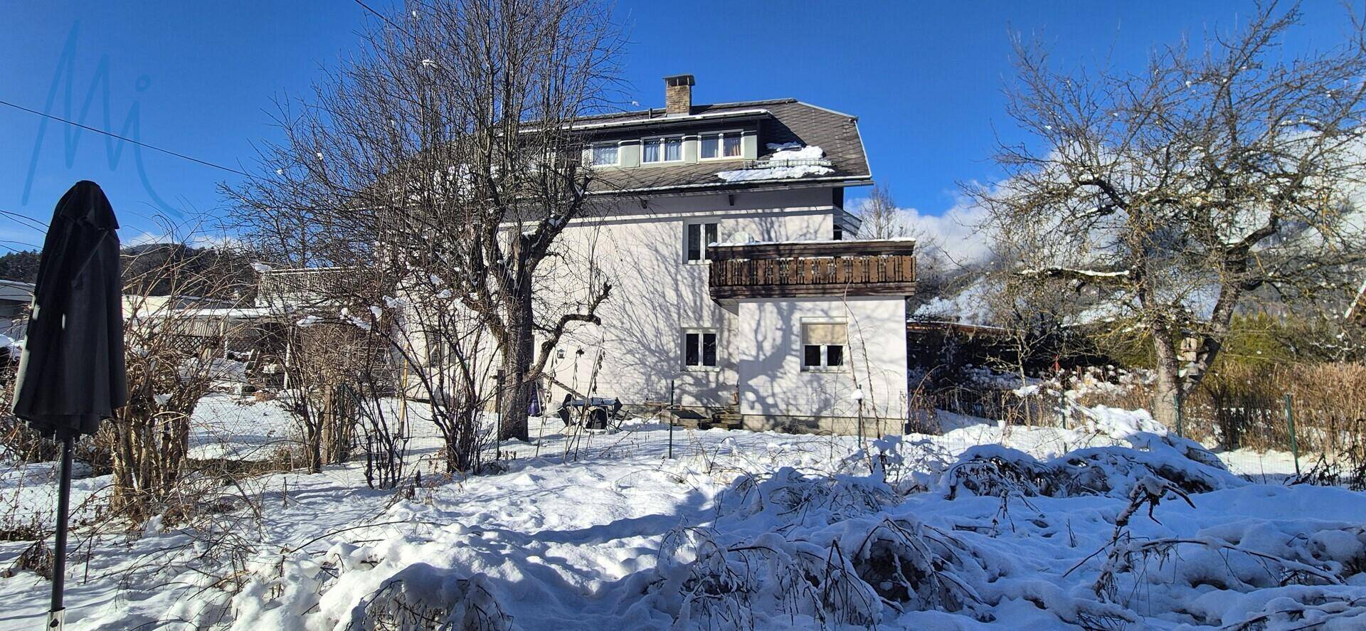 Rückansicht des Hauses im Winter mit schneebedecktem Garten und kahlen Bäumen.