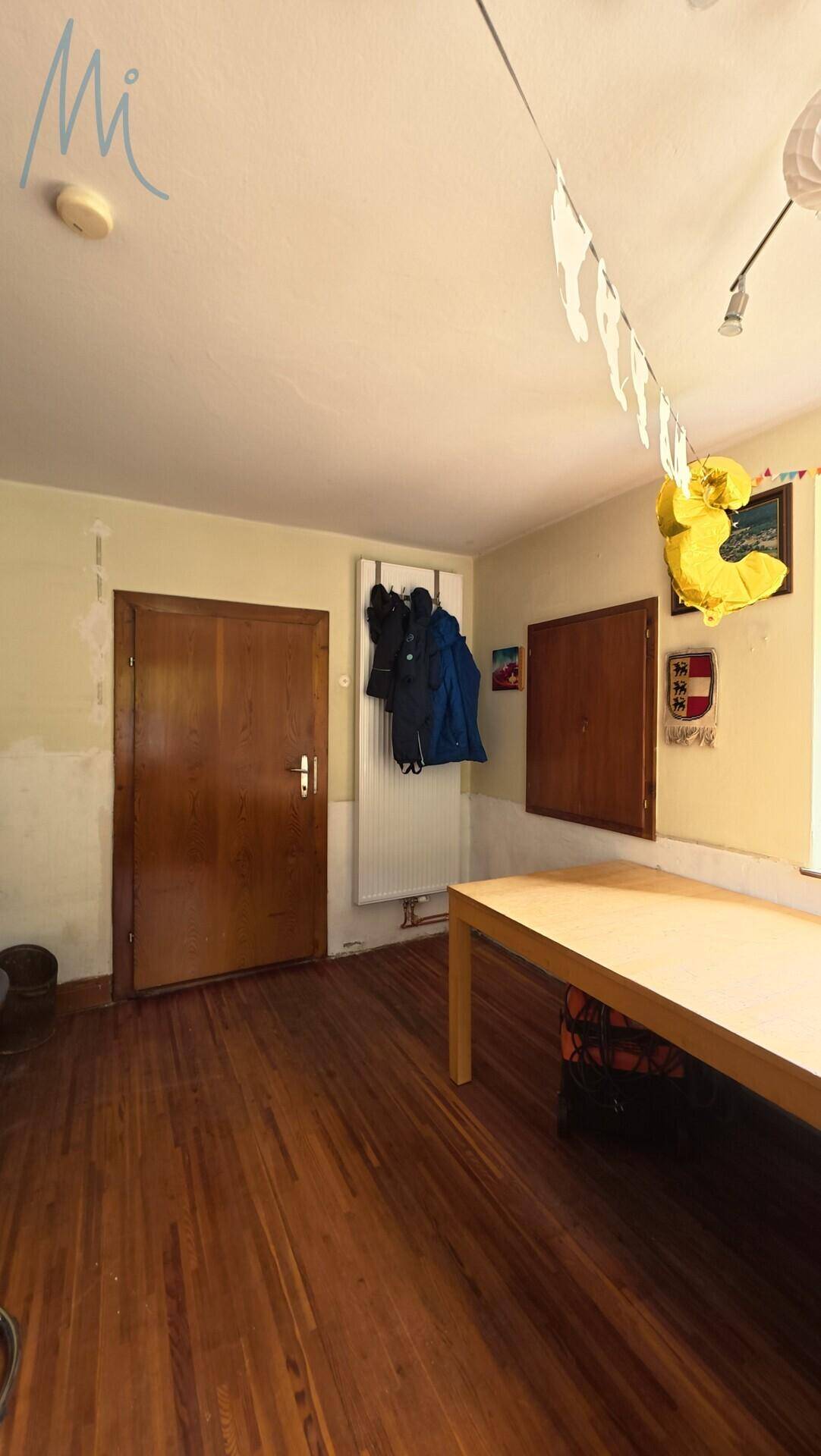 Raum mit Holzboden und einem Holztisch, der als Essbereich oder Mehrzweckraum genutzt werden kann.