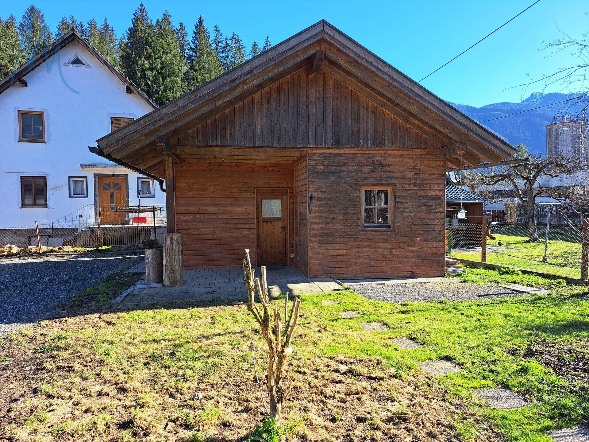 Holzschuppen mit kleiner Rasenfläche und dem Hauptgebäude im Hintergrund.