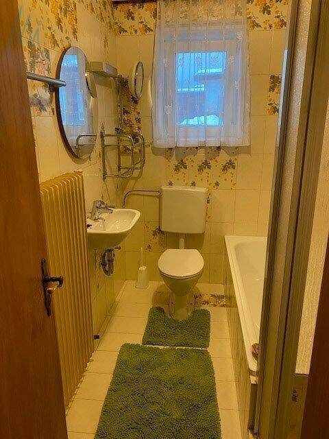 Badezimmer im 80er-Jahre-Stil mit Badewanne, WC, Waschbecken und gemusterter Tapete.