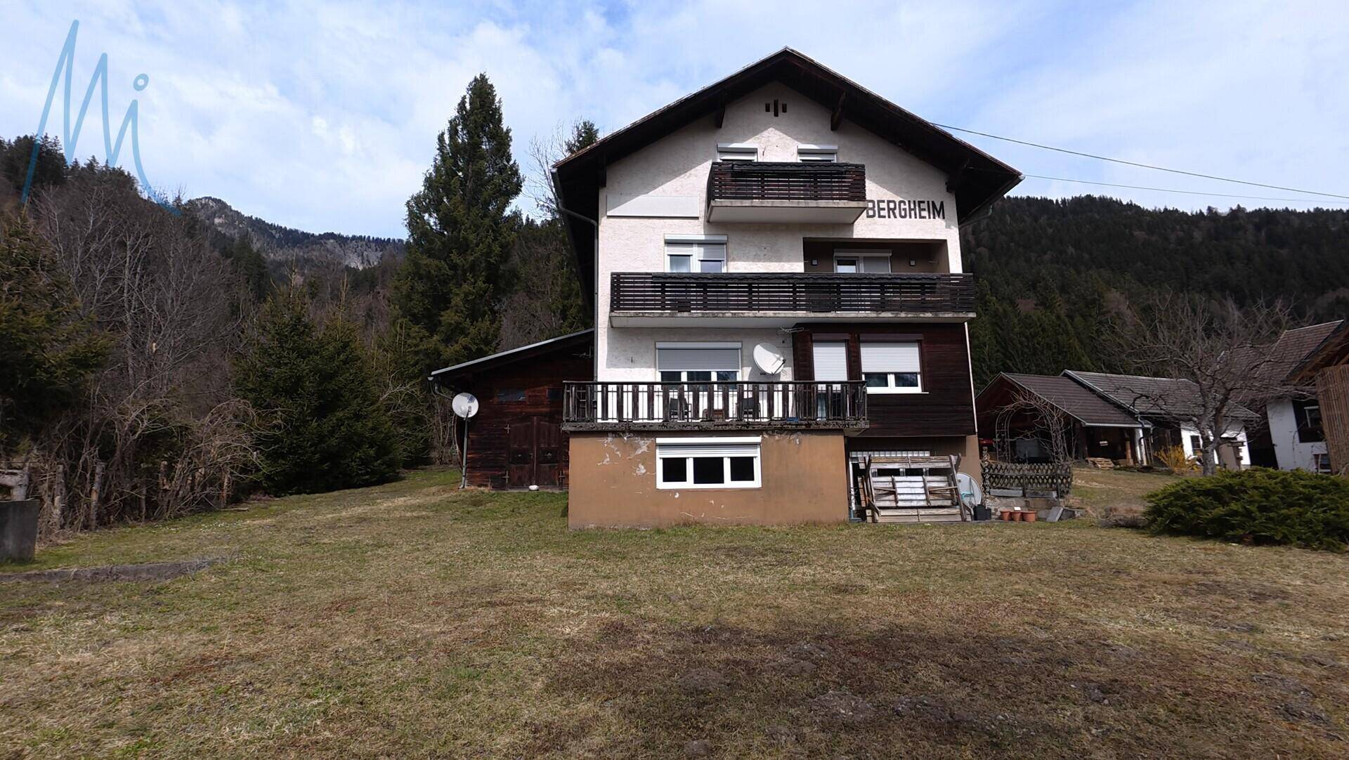 Vorderansicht des Wohnhauses mit Balkonen und großem Gartenbereich.