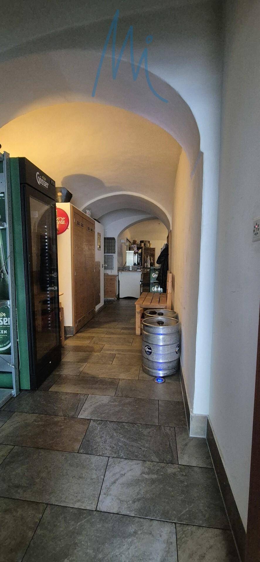 Langer Flur mit gewölbter Decke, Fliesenboden und Getränkekühlern, führt zu weiteren Räumen.