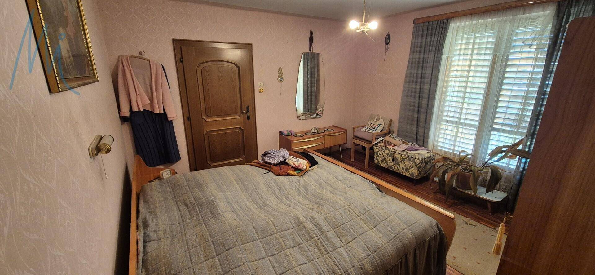 Gemütliches Schlafzimmer mit Doppelbett, Holzmöbeln und einem Fenster mit Jalousien.