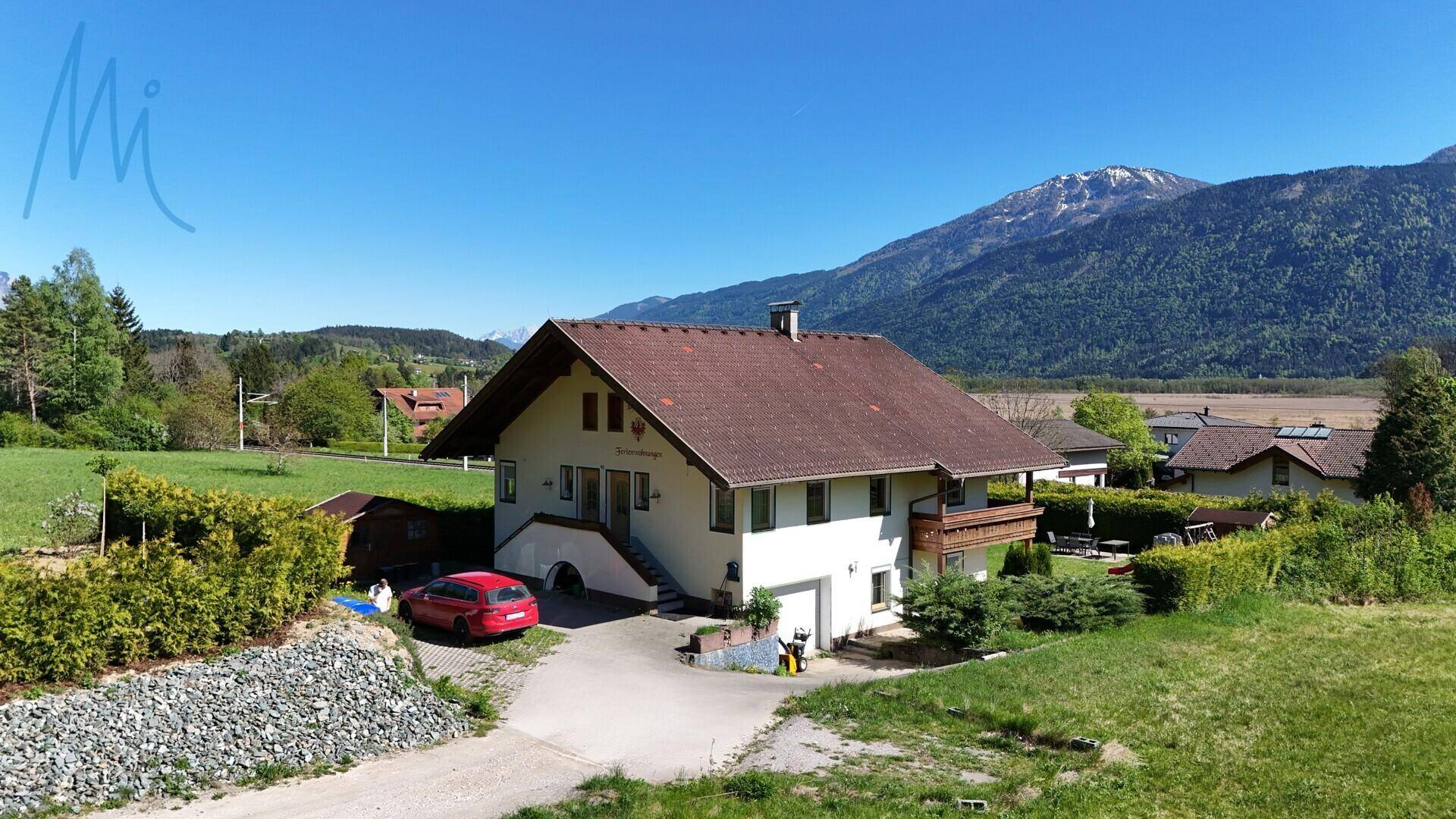 Haus in ländlicher Umgebung mit rotem Auto auf der Auffahrt und beeindruckendem Bergblick.