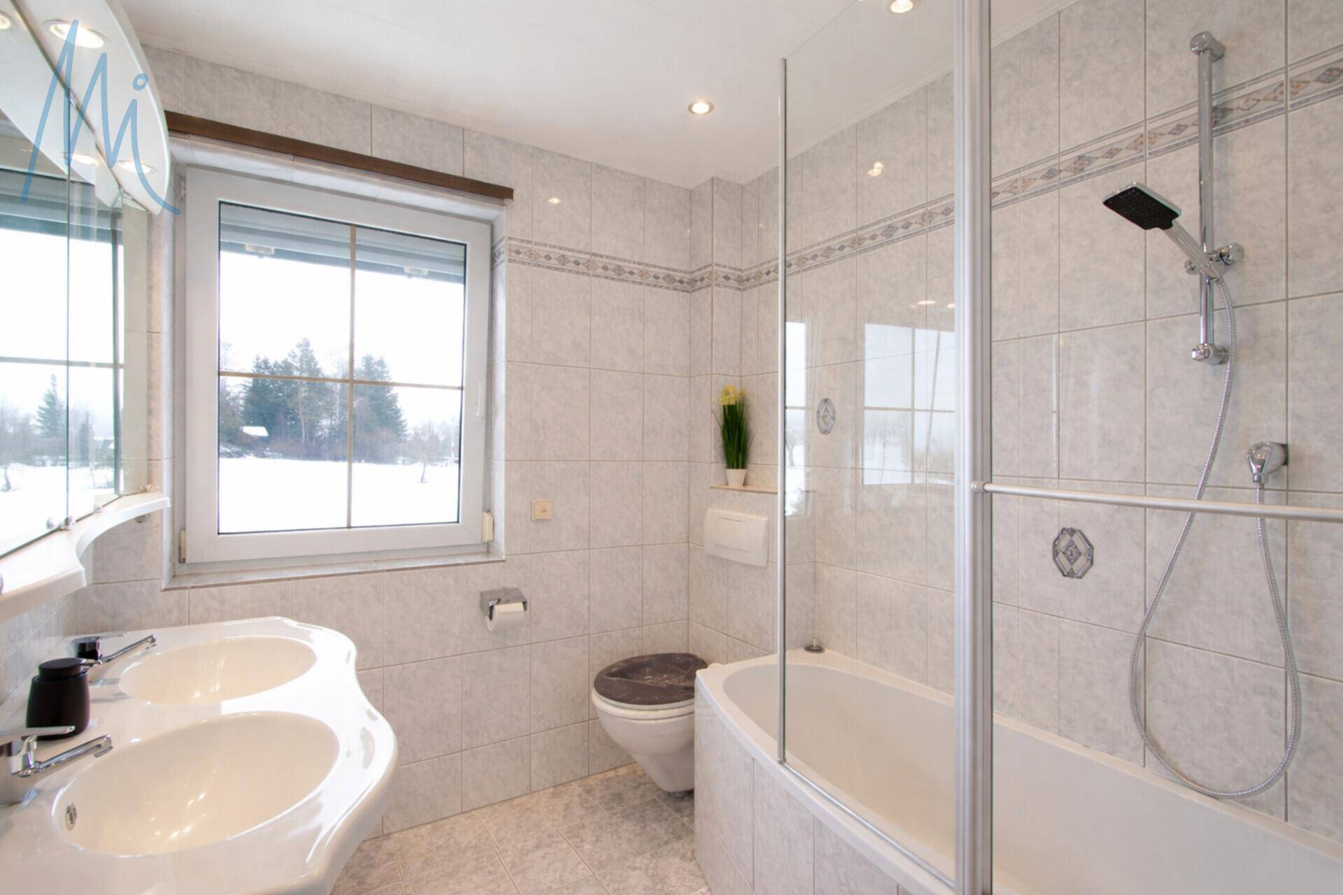 Gefliestes Badezimmer mit Doppelwaschbecken, Badewanne und Duschabtrennung.
