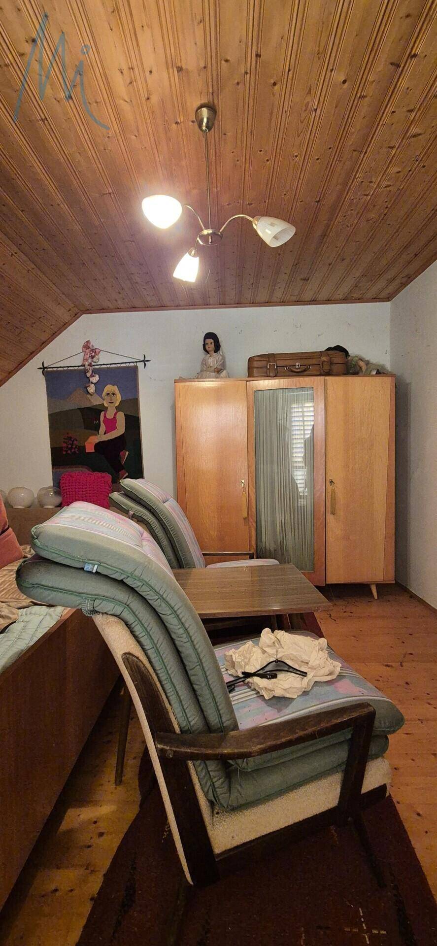 Zimmer mit Holzdecke, Sitzgelegenheiten und einem Kleiderschrank, ideal als Gästezimmer.