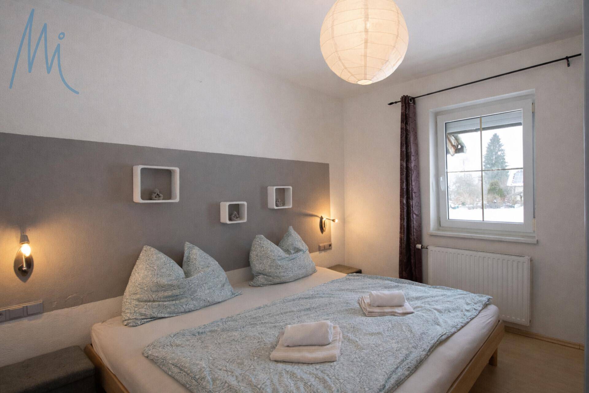 Gemütliches Schlafzimmer mit Doppelbett, grauer Akzentwand und Fenster mit Ausblick.