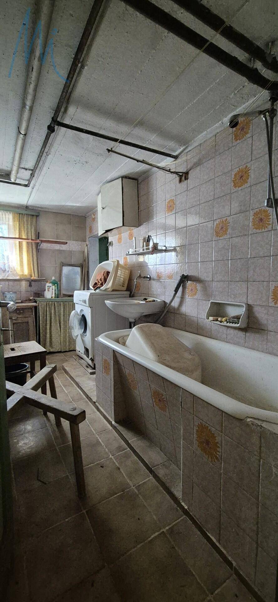 Badezimmer mit Badewanne, Waschbecken und Waschmaschine, gekennzeichnet durch ältere Fliesen und sichtbare Rohre.